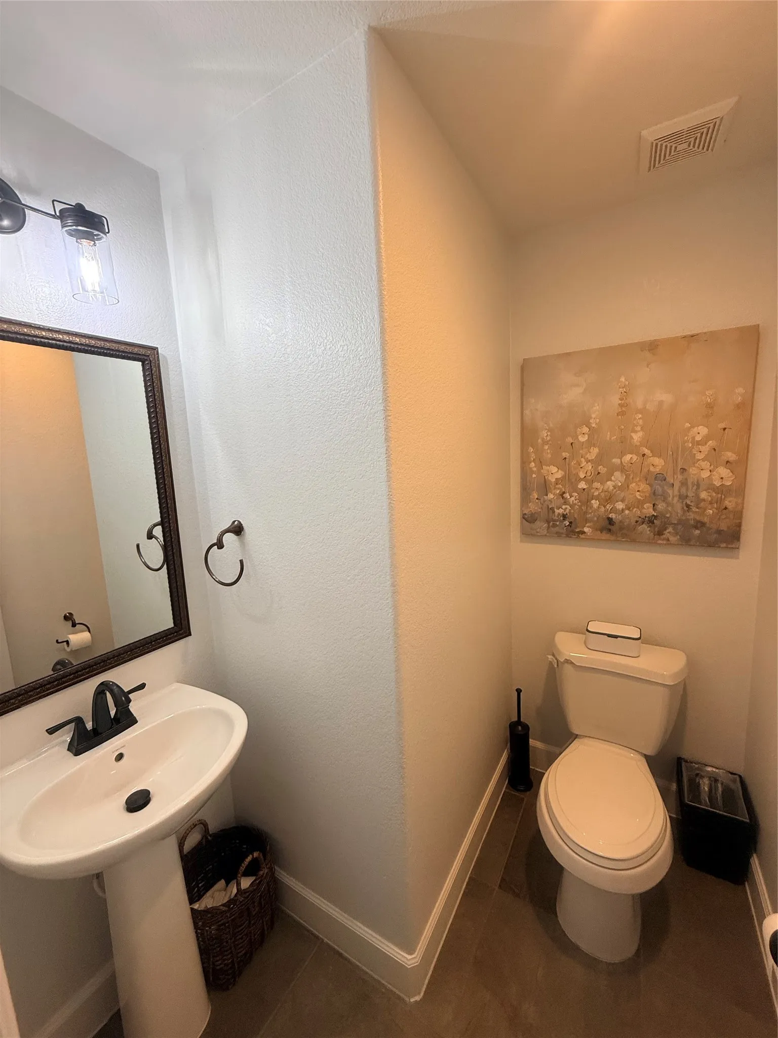 Pedestal sink with dark bronze faucet, framed mirror, and coordinating wall-mounted light fixture