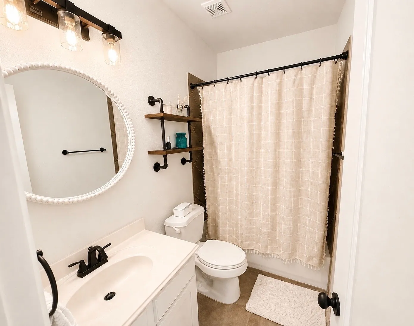 Bathroom featuring a white vanity with a single basin sink and matte black faucet, a round mirror with a beaded frame, and overhead lighting with clear glass shades