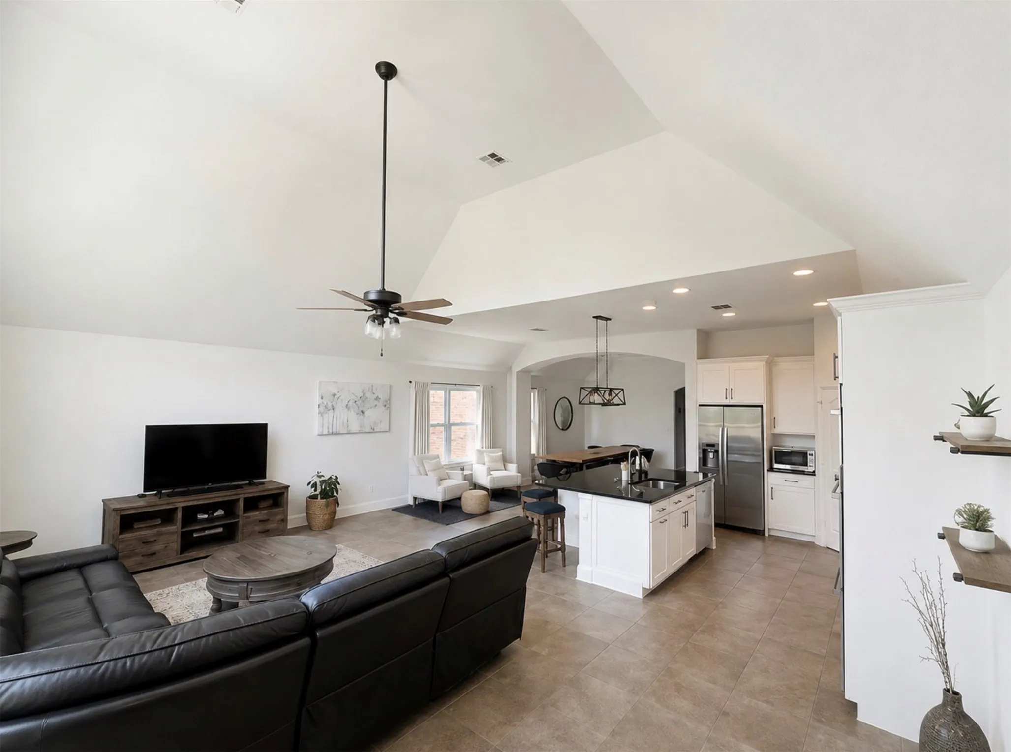 Spacious living area featuring a vaulted ceiling and tile flooring, opening to a kitchen with a large island, white cabinetry, and stainless steel appliances