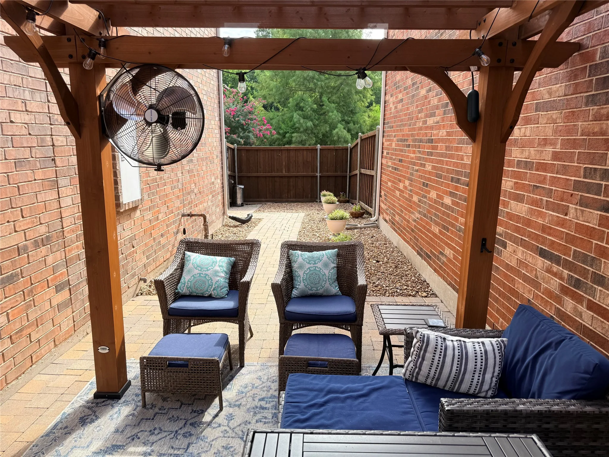 Outdoor patio featuring a wooden pergola with string lighting and a wall-mounted fan
