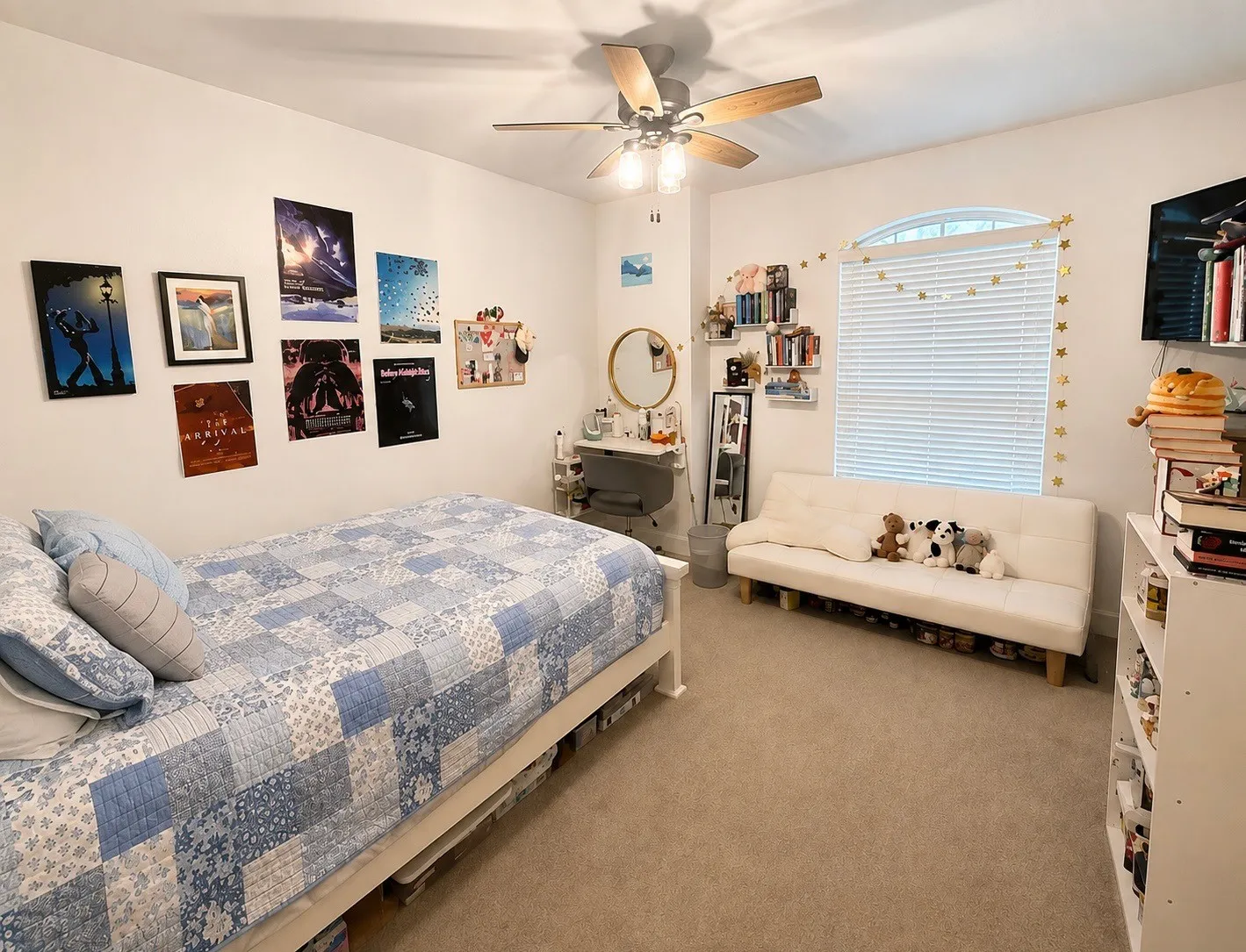 Carpeted room featuring a ceiling fan with light fixture, arched window with horizontal blinds, built-in wall shelving, and a wall-mounted television