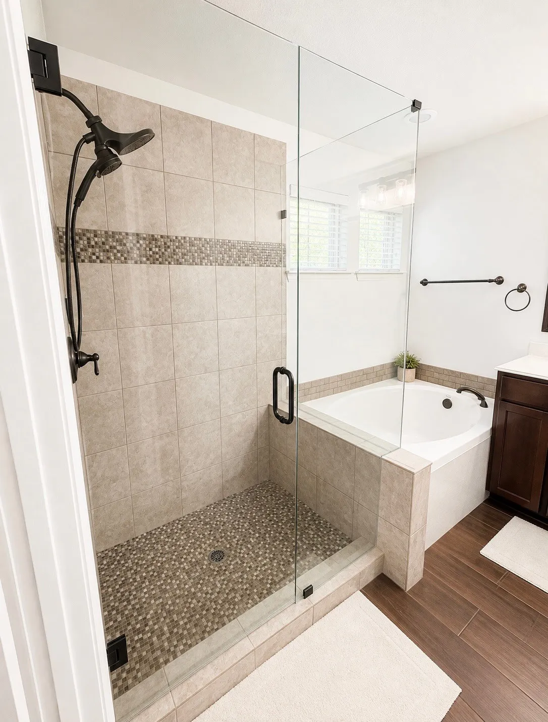 Frameless glass shower enclosure featuring tile walls with a mosaic accent band, pebble floor, and a dark bronze shower fixture