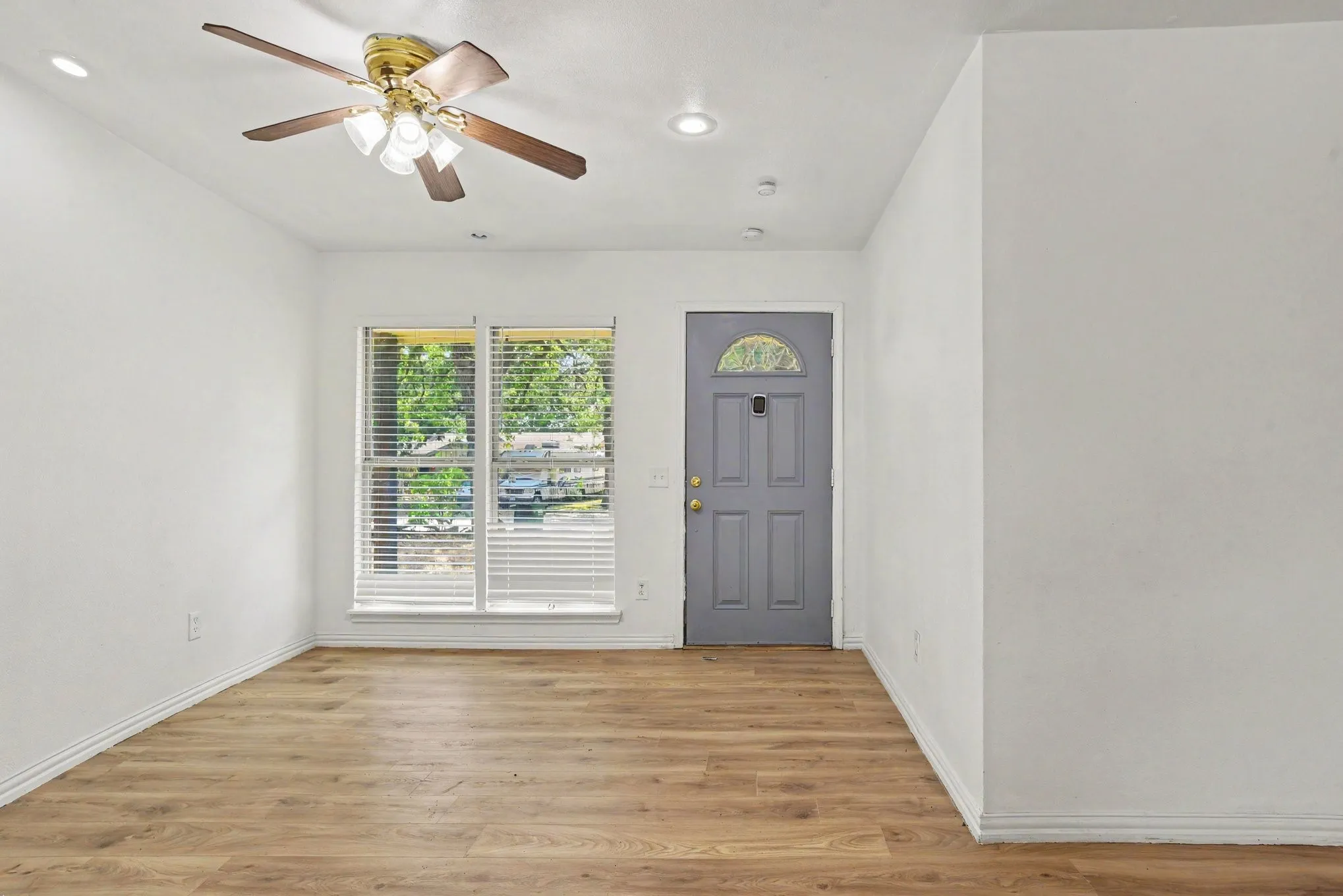 Bright front entry space featuring light wood-look flooring, fresh white walls, ceiling fan, and blue accent front door.