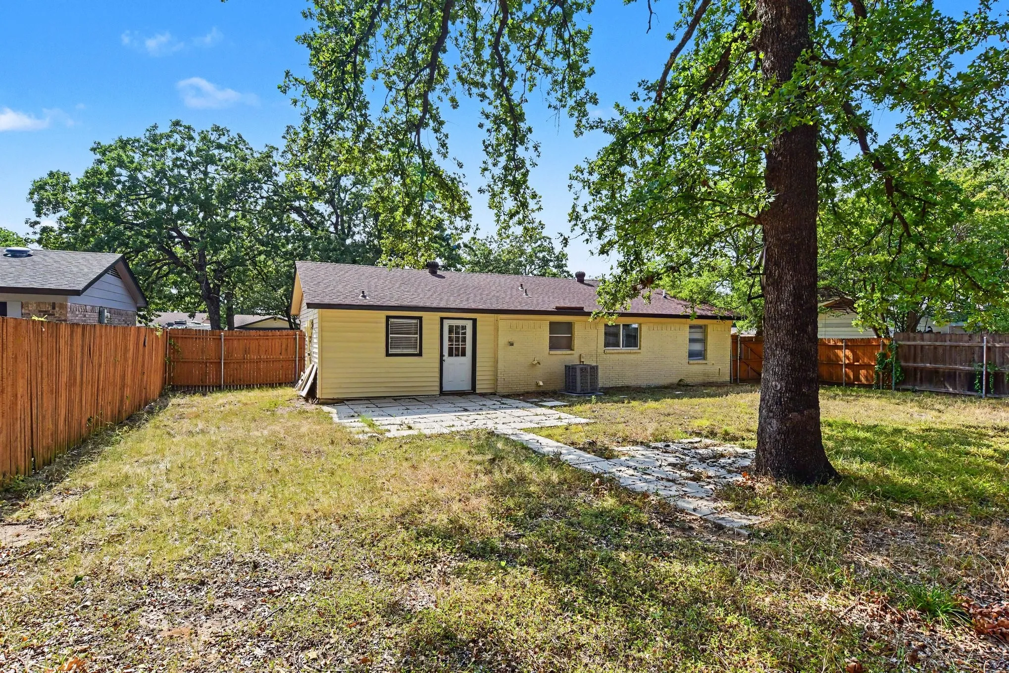 Angled exterior view showing the full length of the home, front yard, and surrounding mature foliage.
