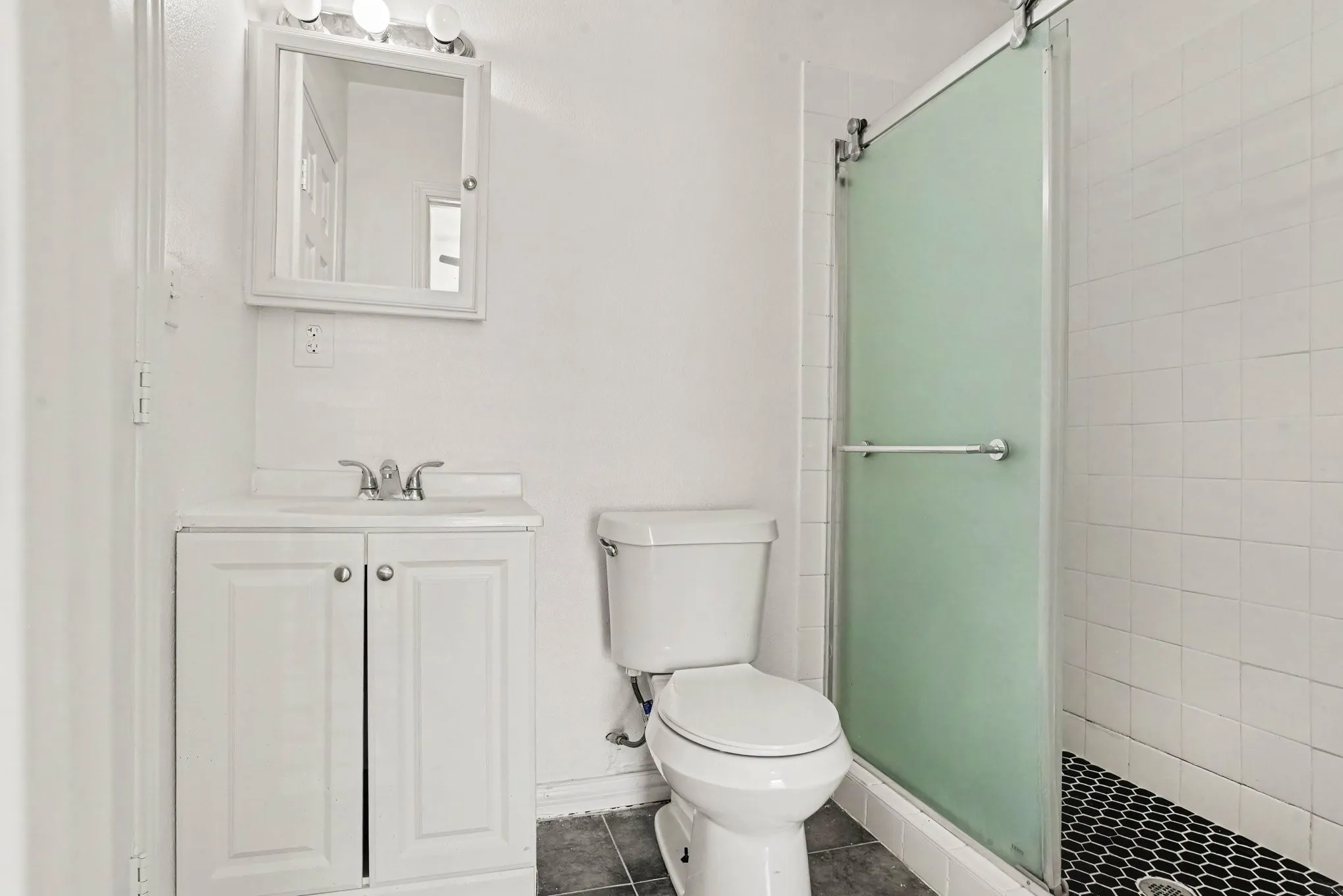 Secondary bathroom view showcasing clean white finishes, medicine cabinet, and glass shower enclosure.