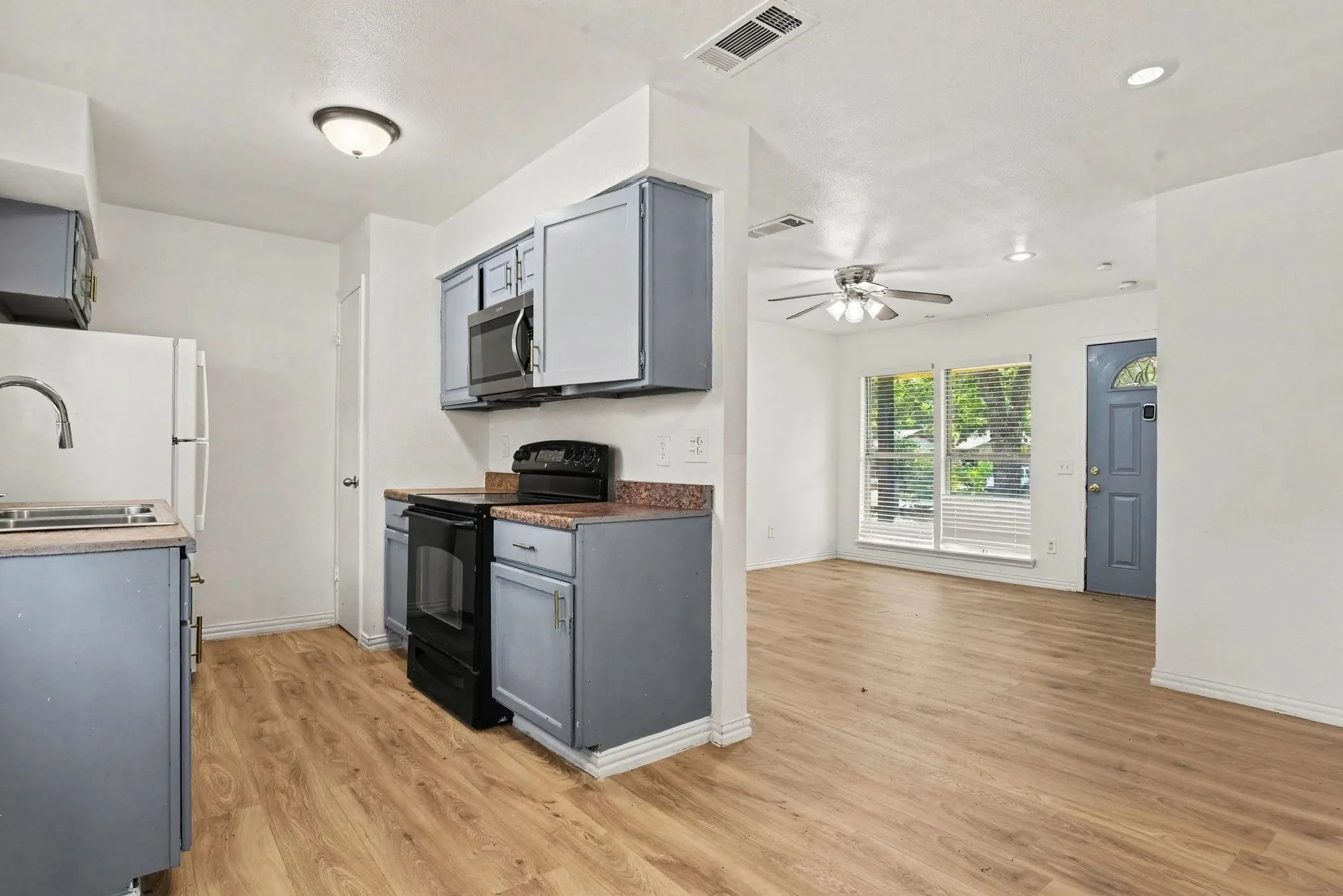 Galley kitchen featuring grey cabinetry, stainless steel microwave and range, and bright dining space access.