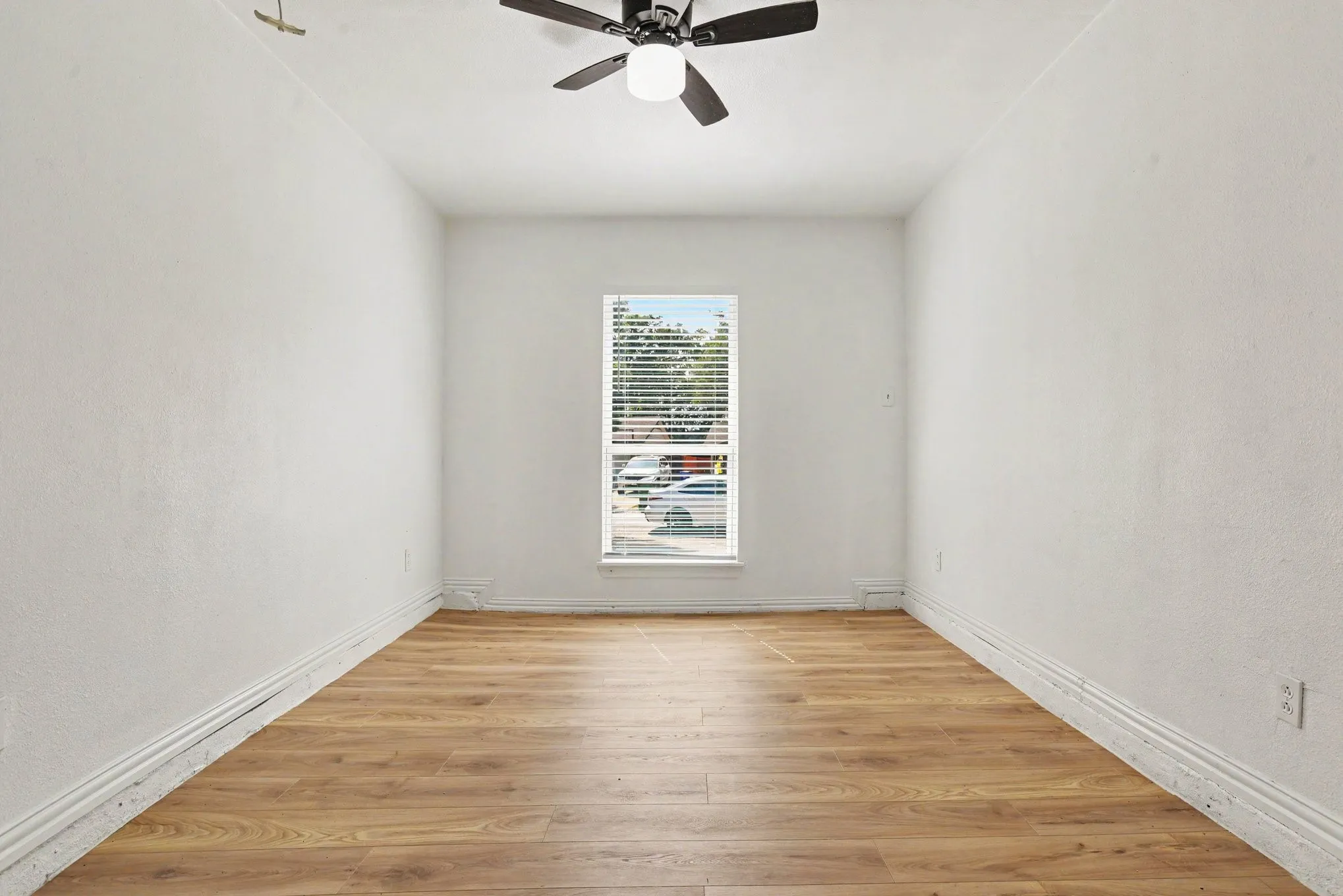 Versatile bedroom or home office space with central window lighting and ceiling fan.