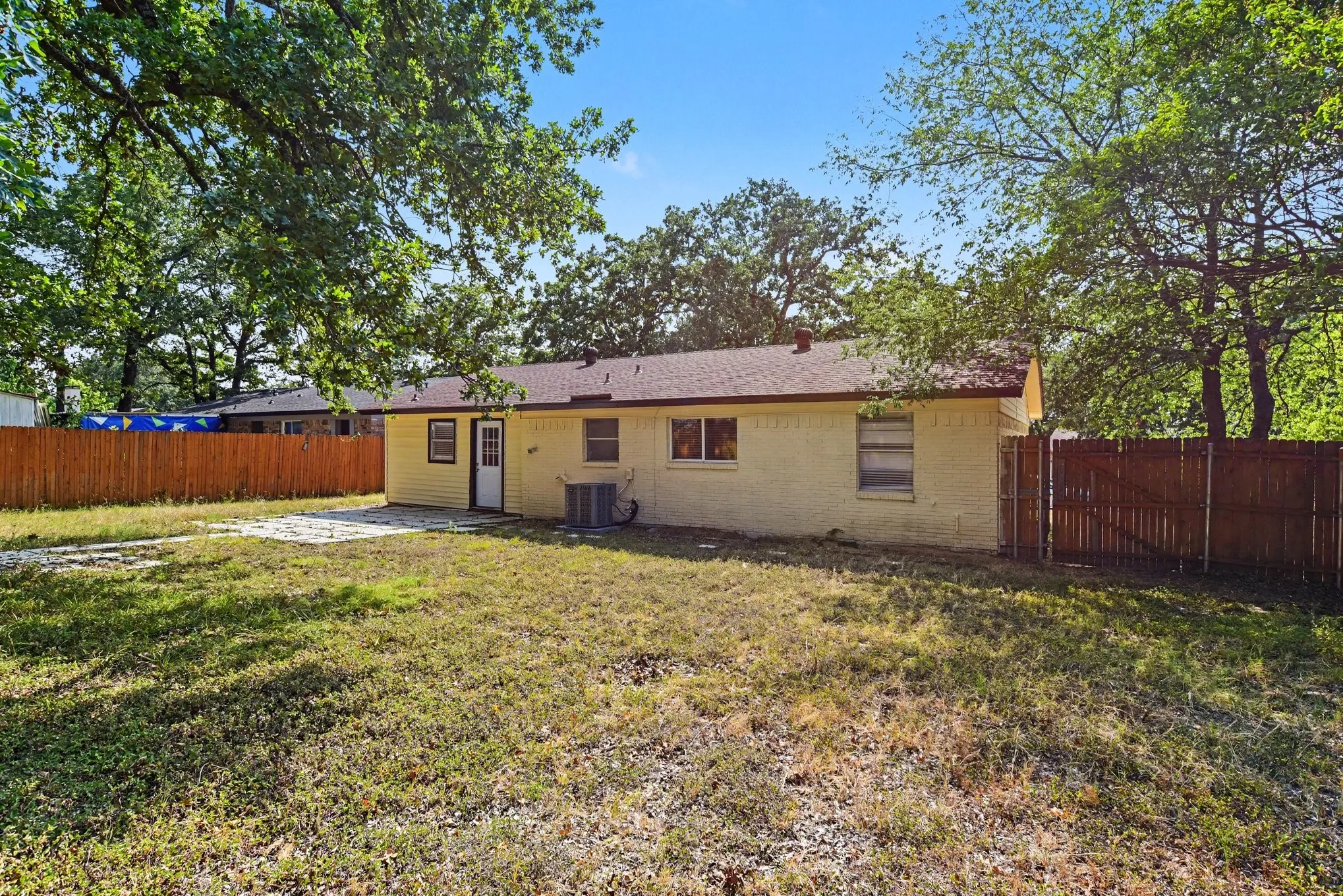 Full rear exterior view of the house showing the back elevation, fenced lawn, and tree canopy.