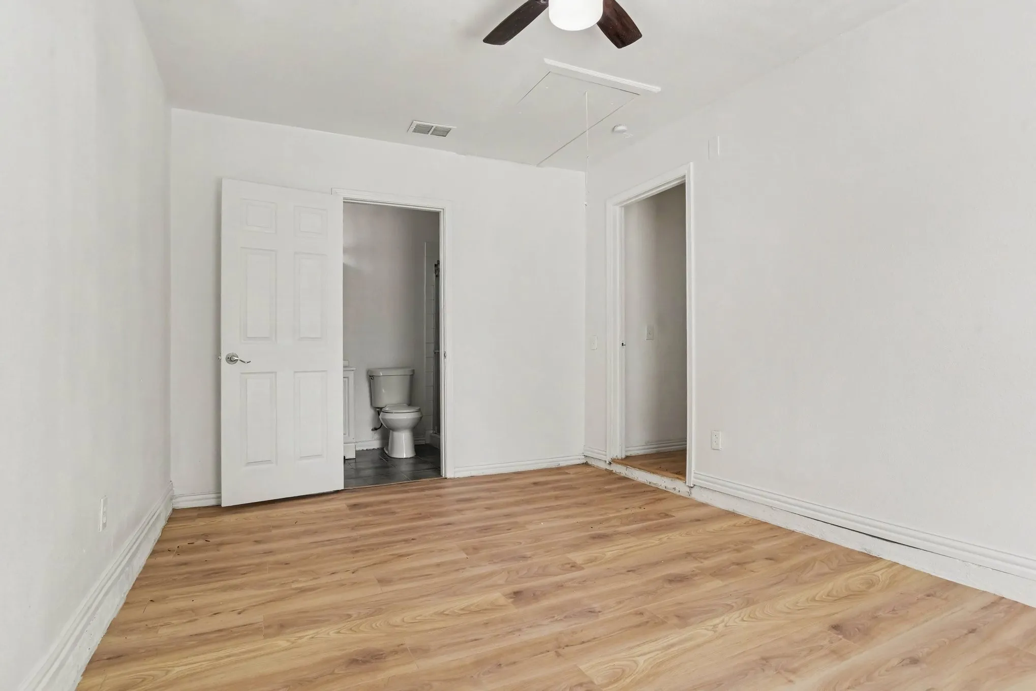 Primary bedroom with light wood-tone flooring, ceiling fan, and generous wall space.