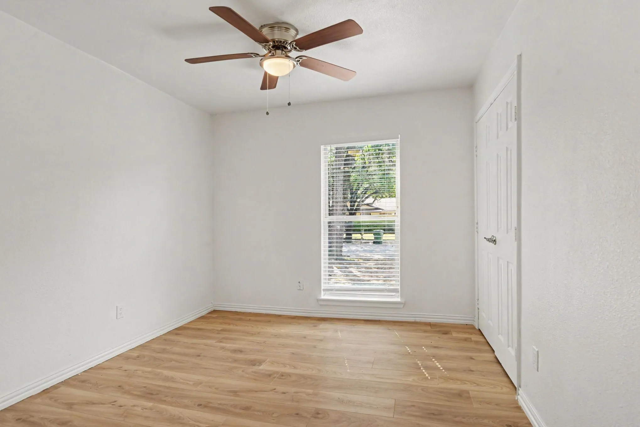 Secondary bedroom filled with natural light from a large single window, featuring wood-look floors.
