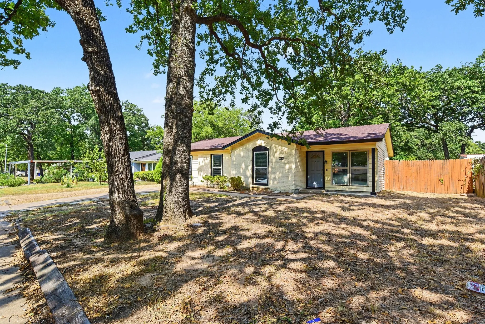 Spacious front yard framed by large shade trees and a fully fenced perimeter.