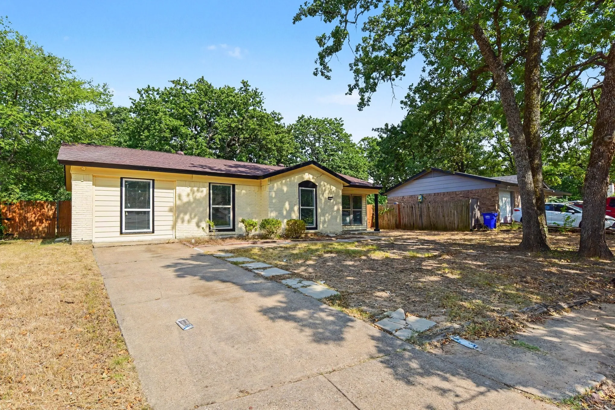 Daytime front view displaying the extended driveway, front entrance, and shaded yard area.