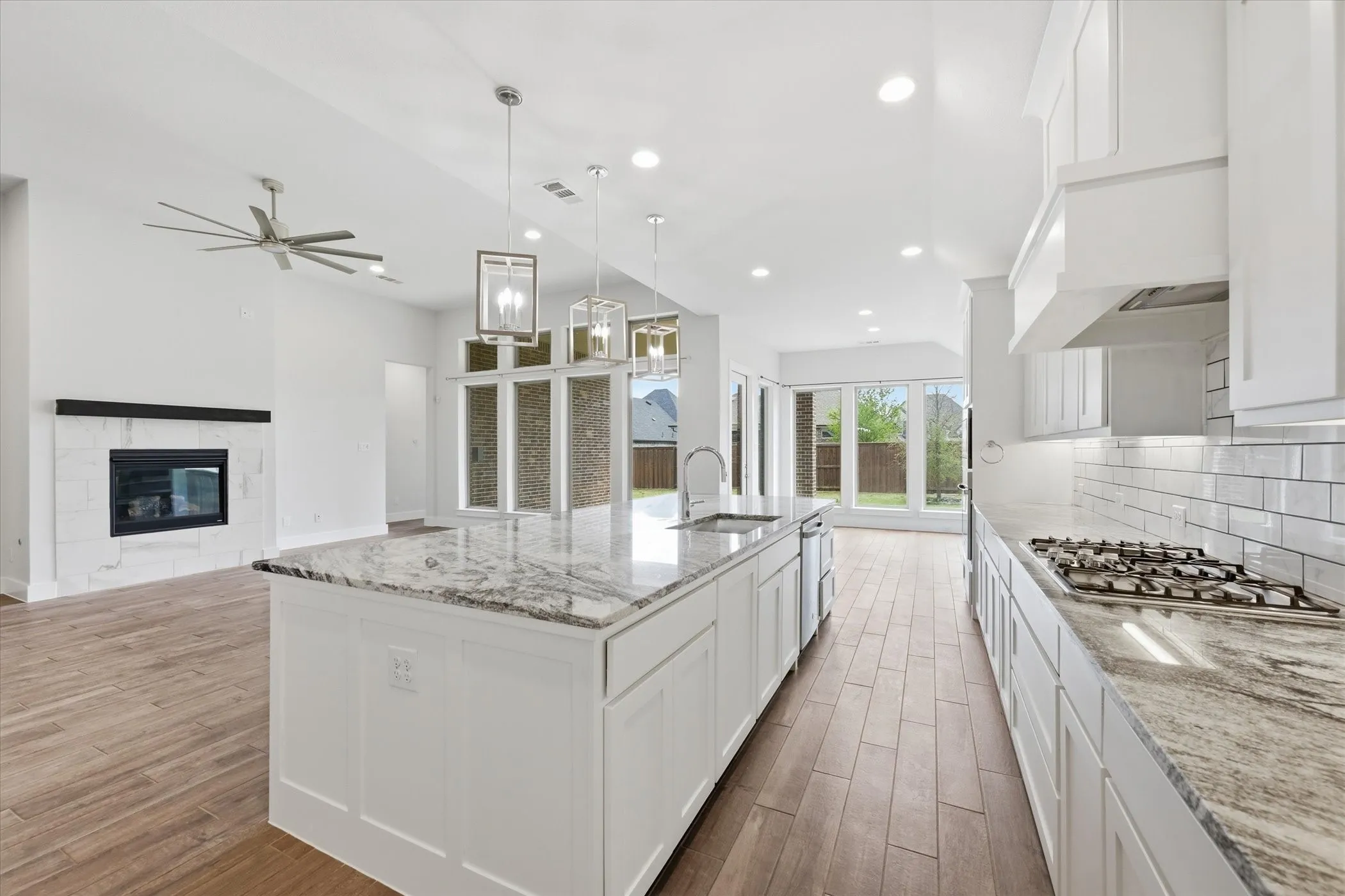 Open-concept interior featuring wood-finish flooring, a kitchen island with stone countertop, stainless steel appliances, and a fireplace with a stone surround