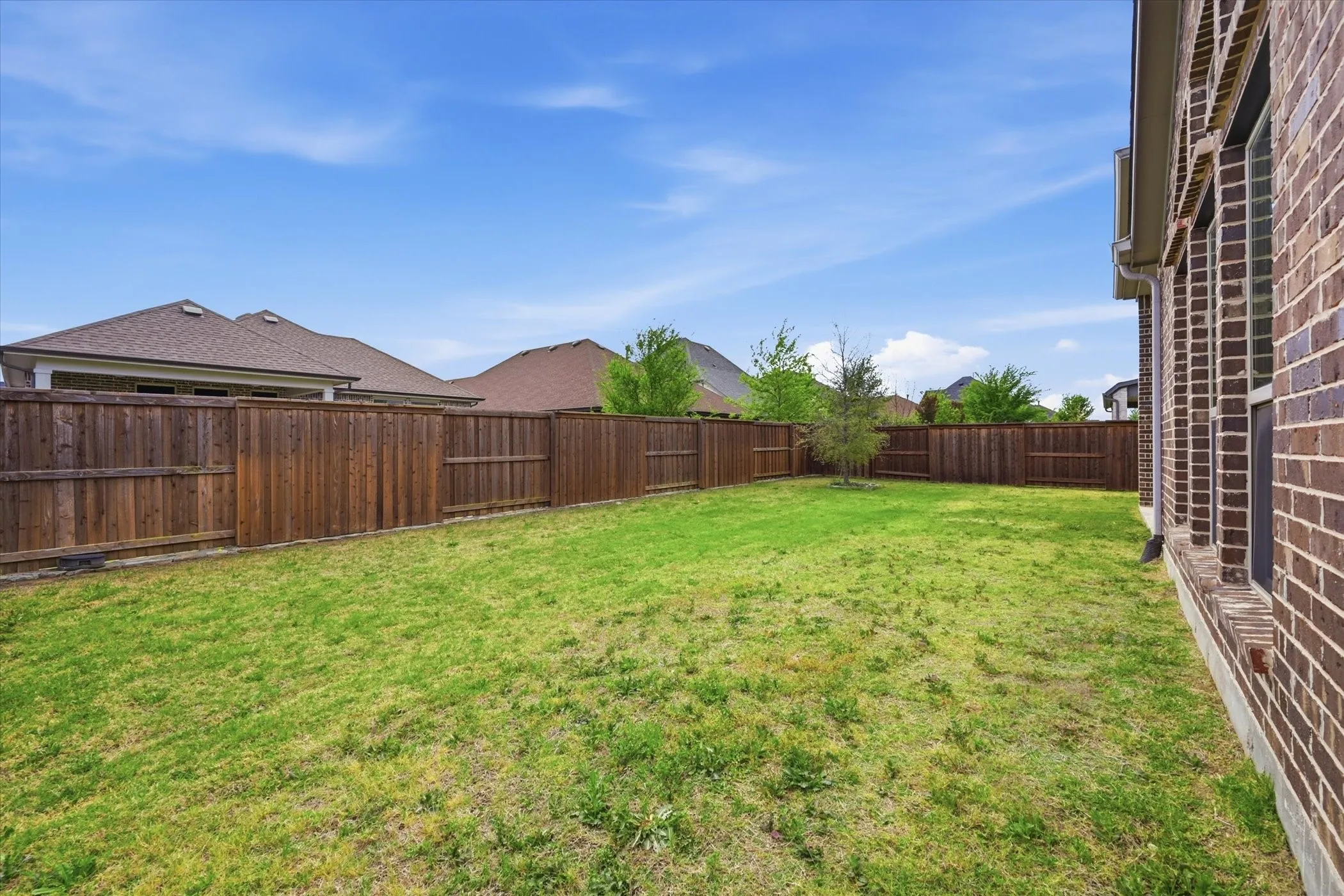 Expansive backyard featuring a manicured lawn, full privacy fencing, and a brick exterior with multiple windows