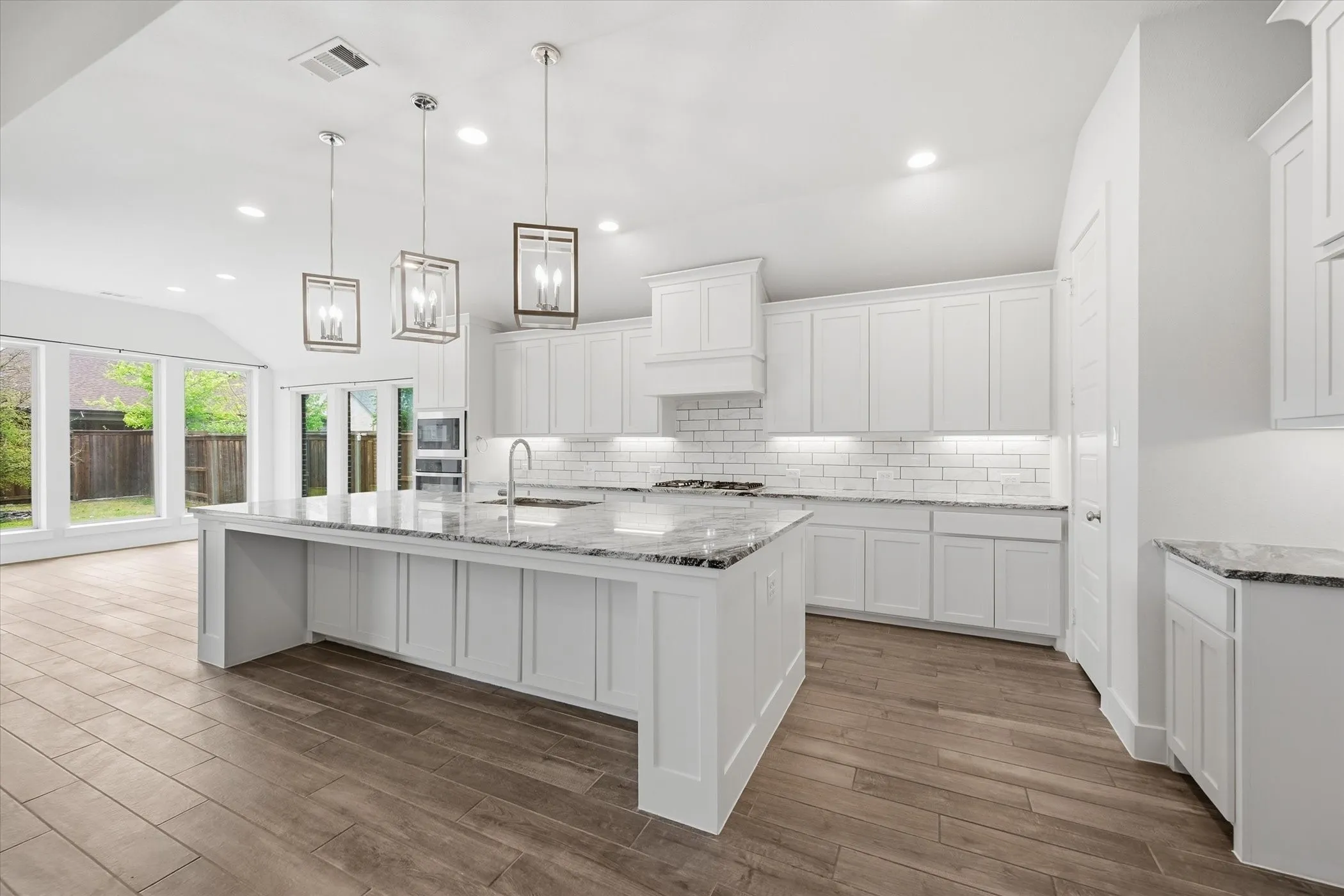 Gourmet kitchen featuring white shaker cabinetry, subway tile backsplash, stainless steel appliances, and an expansive island with a stone countertop