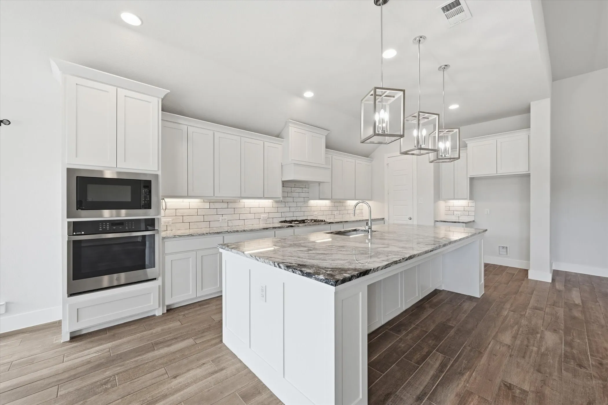 Contemporary kitchen featuring white cabinetry, a large kitchen island with a stone countertop, built-in stainless steel appliances, and wood-finish flooring