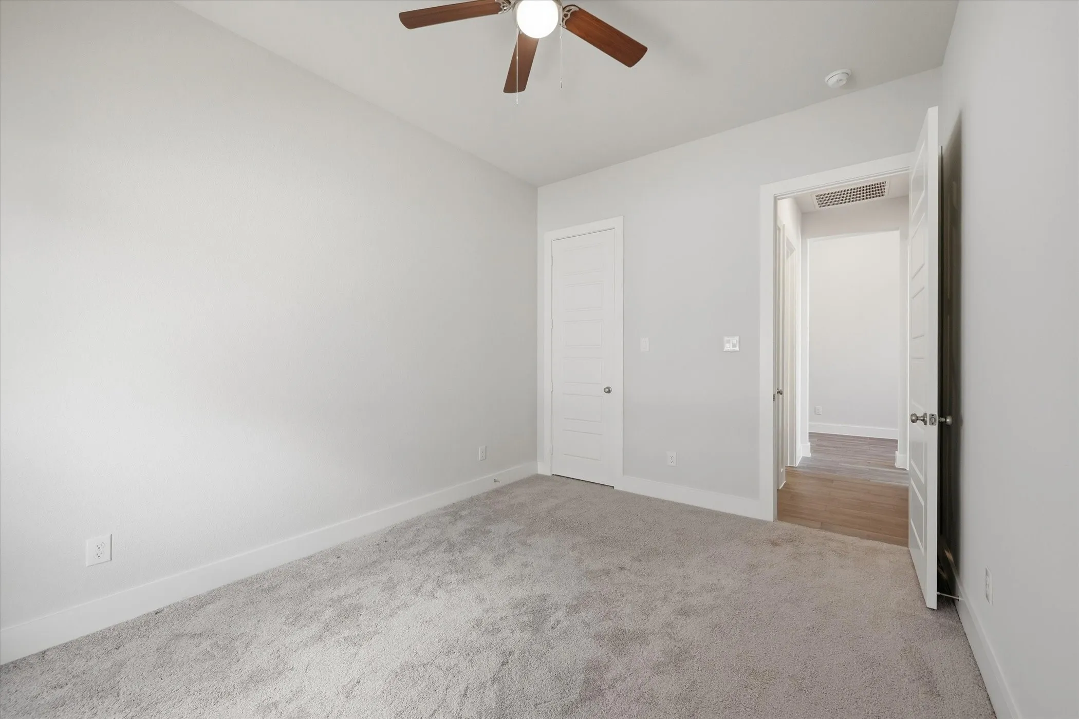 Neutral-toned walls, gray carpet flooring, ceiling fan with wood-finish blades, white paneled doors, and white trim