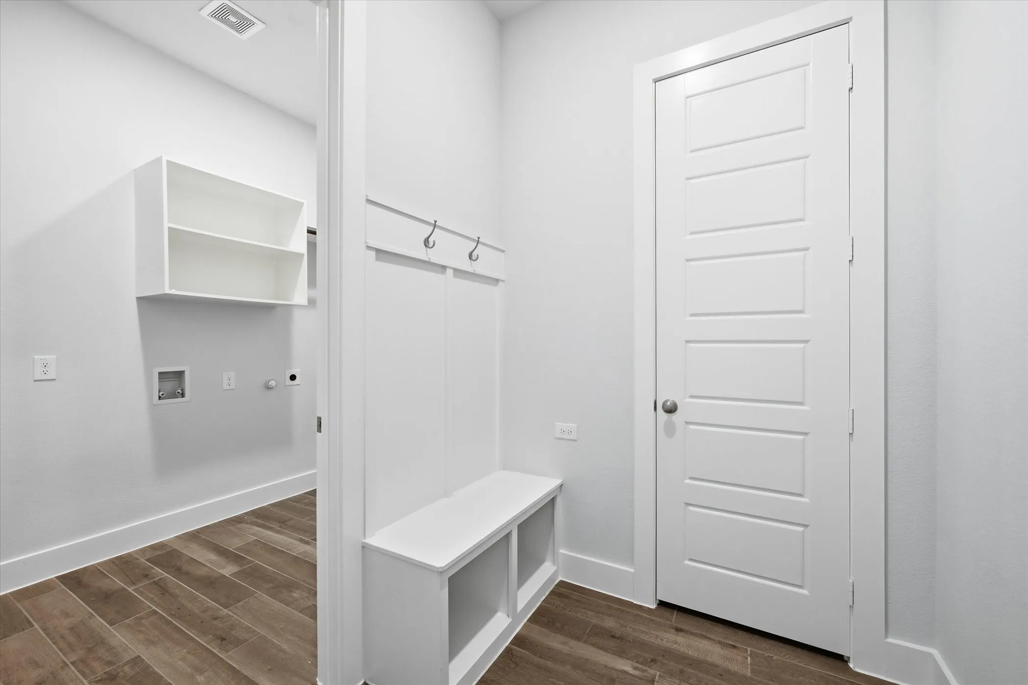 Built-in bench with storage, peg hooks, white paneled door, wood-finish flooring, and wall-mounted​​‌​​​​‌​​‌‌​‌‌​​​‌‌​‌​‌​‌​​​‌​​ shelving