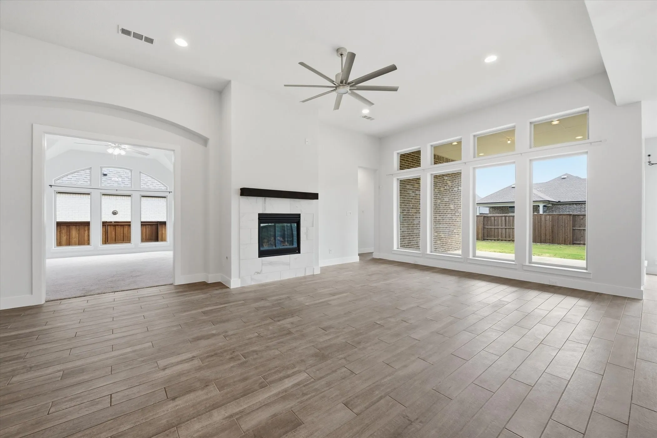 Wood-finish plank flooring, modern fireplace with a white surround and dark mantel, high ceilings, recessed lighting, and a contemporary ceiling fan