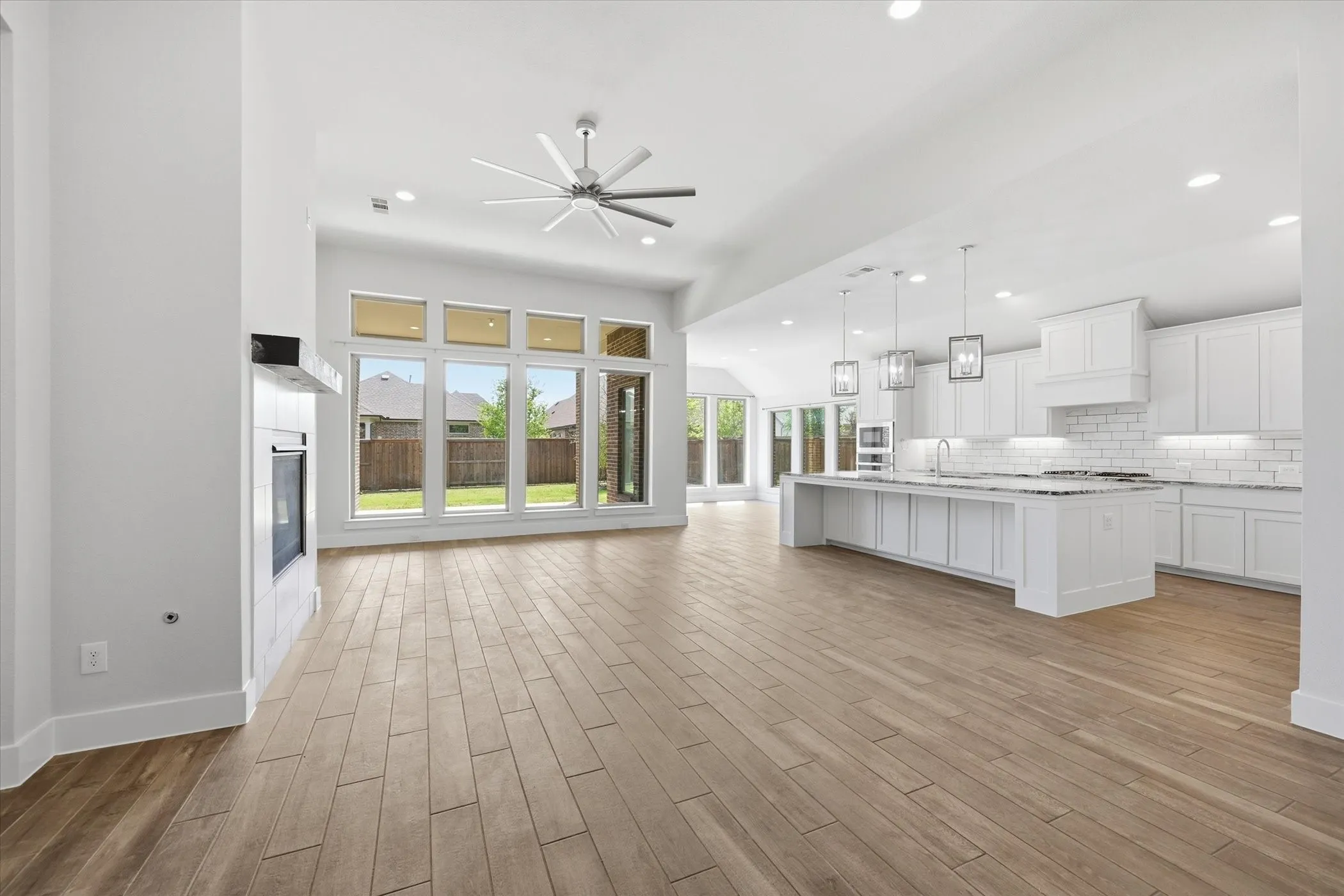 Open-concept living area with vaulted ceilings, a built-in fireplace, wood-finish flooring, and expansive windows