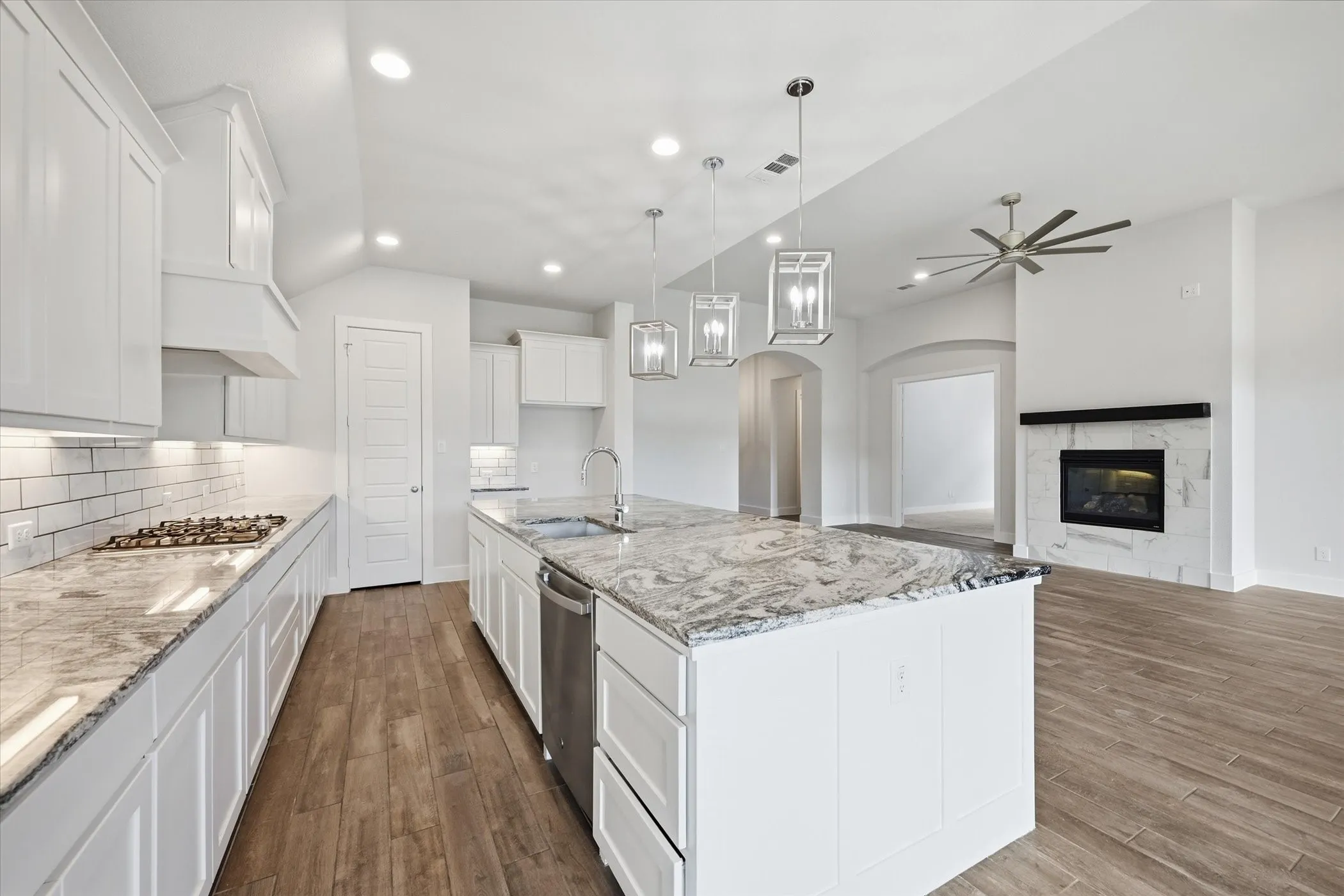 Chef's kitchen featuring white cabinetry, a large marble-topped island with waterfall edge, stainless steel appliances including a gas cooktop and built-in wall oven, subway tile backsplash, and pendant lighting