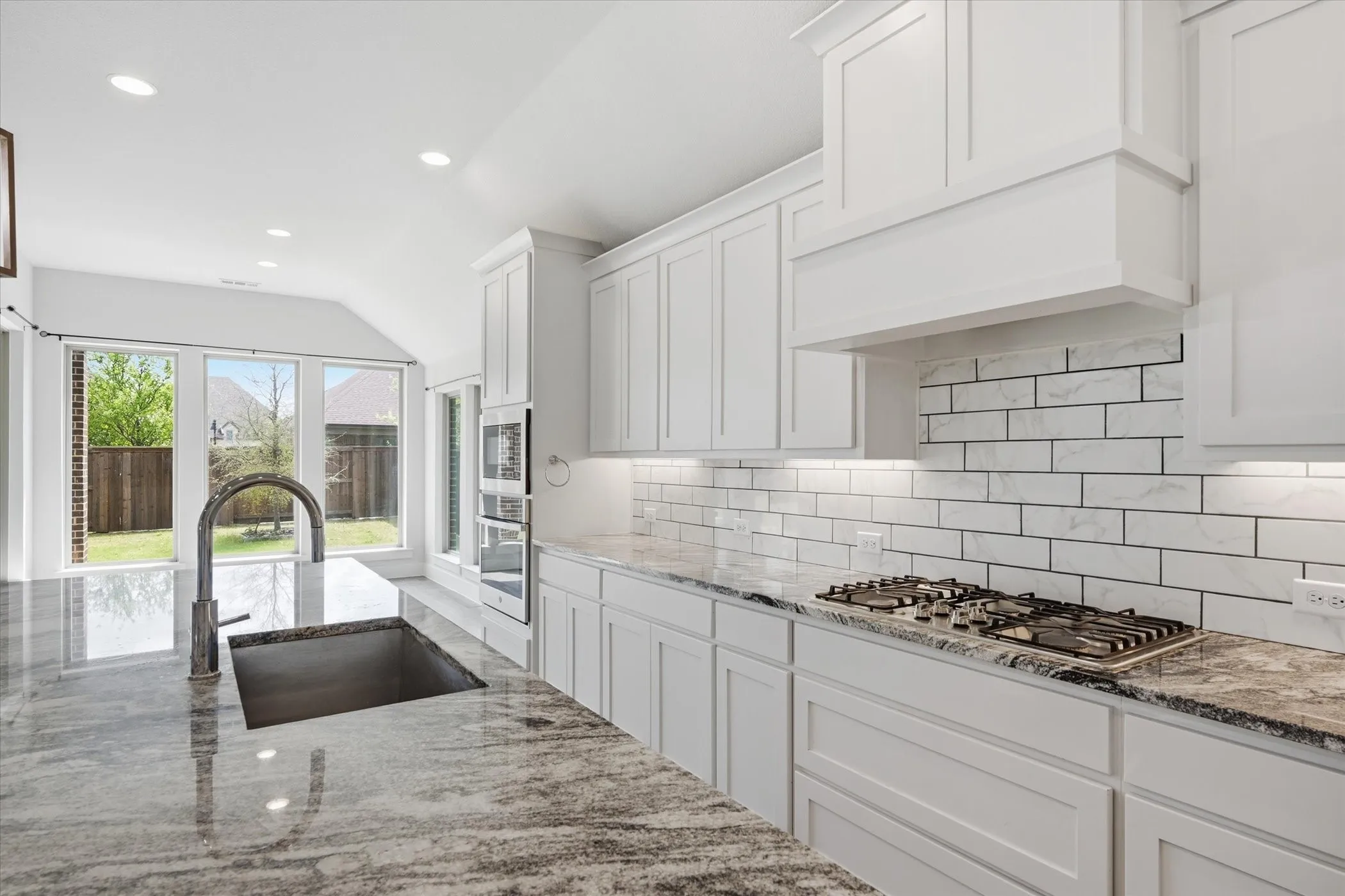 Spacious kitchen featuring white cabinetry, stone countertops, subway tile backsplash, a gas cooktop, and large windows