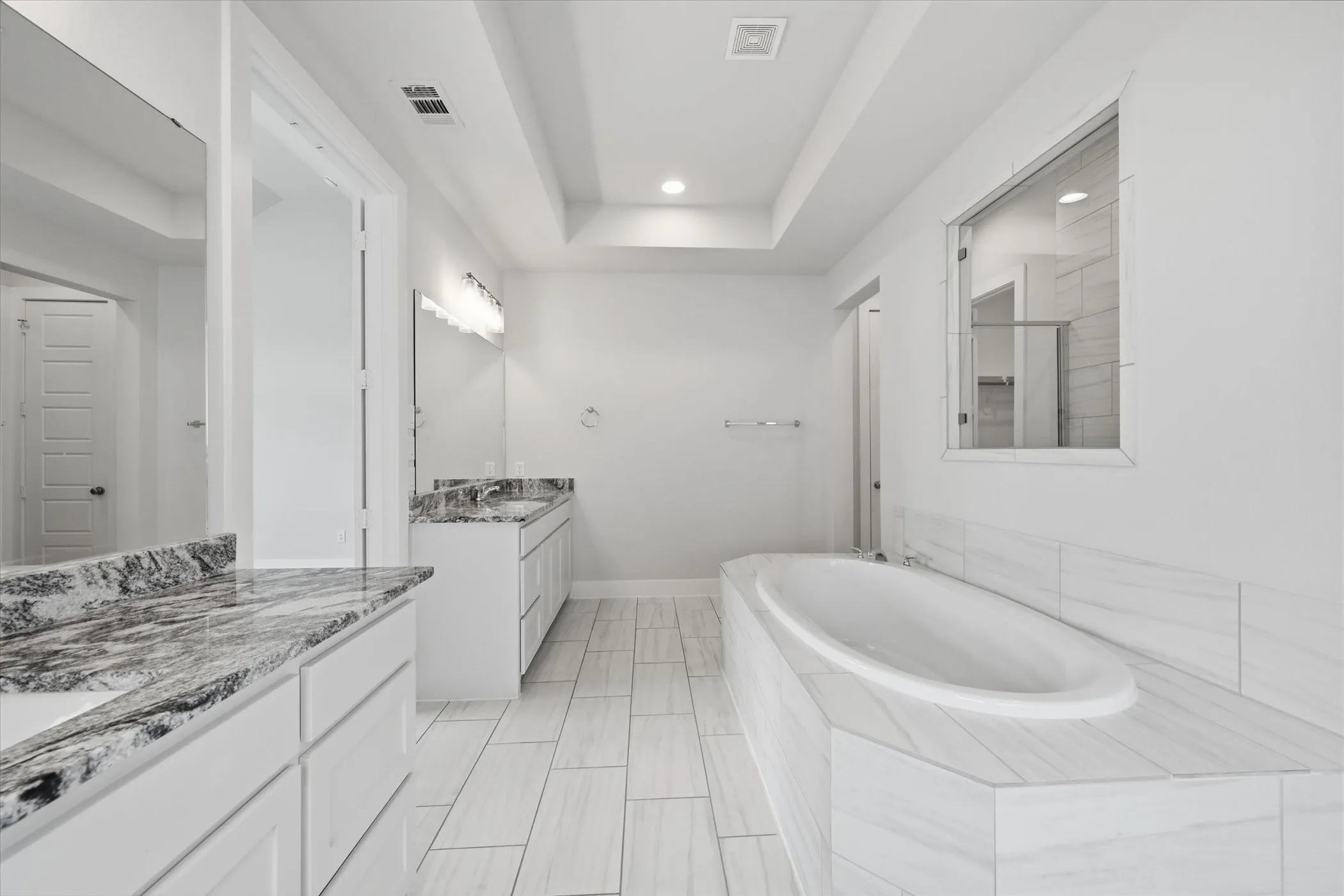 Spa-inspired primary bathroom featuring a freestanding soaking tub, dual-sink vanity with marble-look countertops, frameless glass shower enclosure, recessed ceiling lighting, and light-finish tile flooring throughout