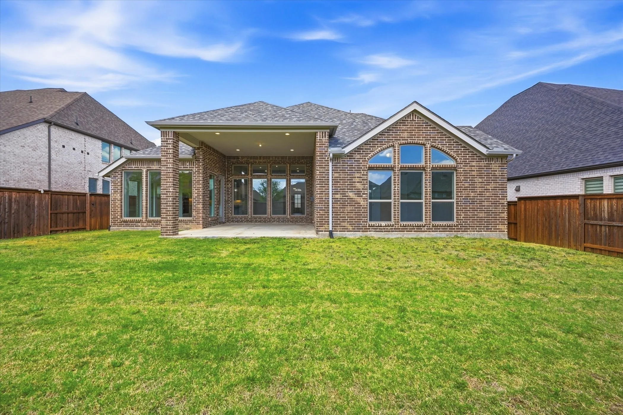 Expansive backyard with a covered patio, brick exterior, multiple large windows, and a privacy fence