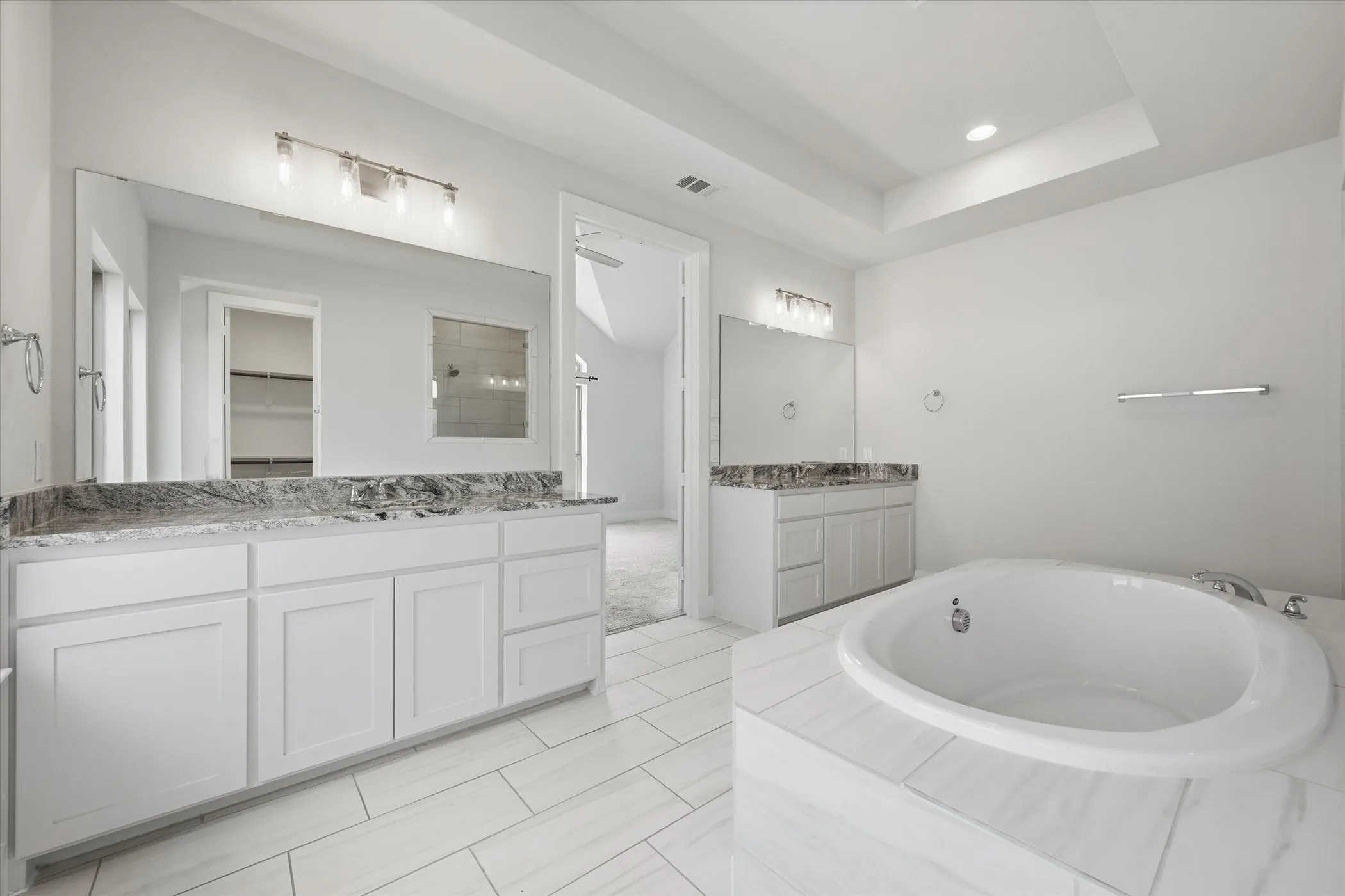 Dual vanity with stone countertops and undermount sinks, integrated soaking tub, tiled flooring, and recessed lighting