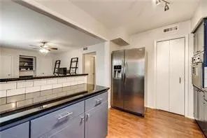 Contemporary kitchen featuring stainless steel appliances, navy cabinetry with polished hardware, white subway tile backsplash, dark countertops, and warm wood-finish flooring throughout the open layout