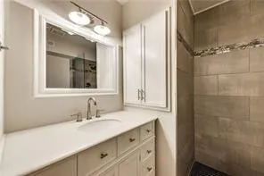 Spa-inspired ensuite bathroom featuring a white cabinetry vanity with multiple drawers, quartz countertop, polished nickel fixtures, and an illuminated mirror with integrated lighting