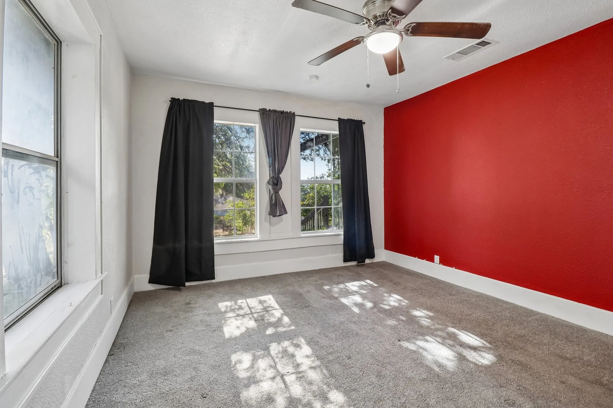Room with a textured red accent wall, gray carpet, and a ceiling fan with light fixture