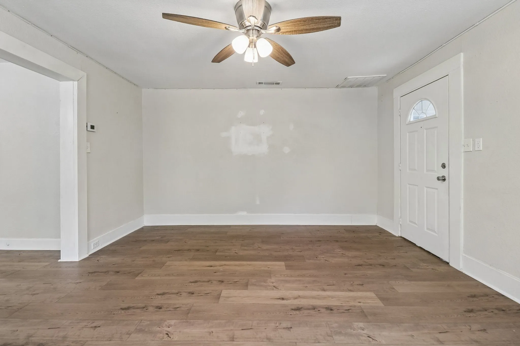 Wood-finish flooring, ceiling fan, white paneled door with arched window, and bright white trim