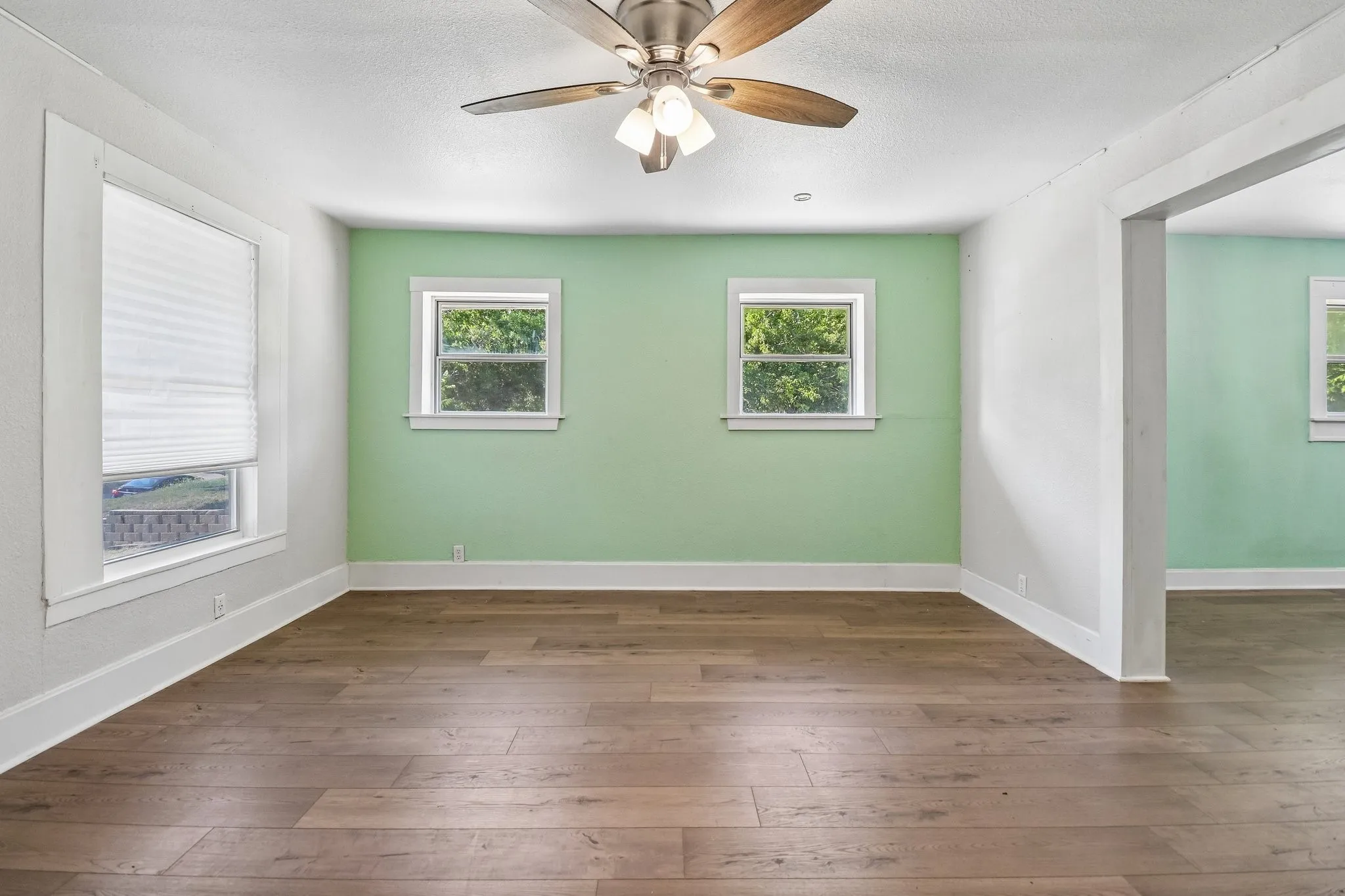 Bright and spacious room showcasing fresh sage green accent walls, white trim, and hardwood flooring throughout