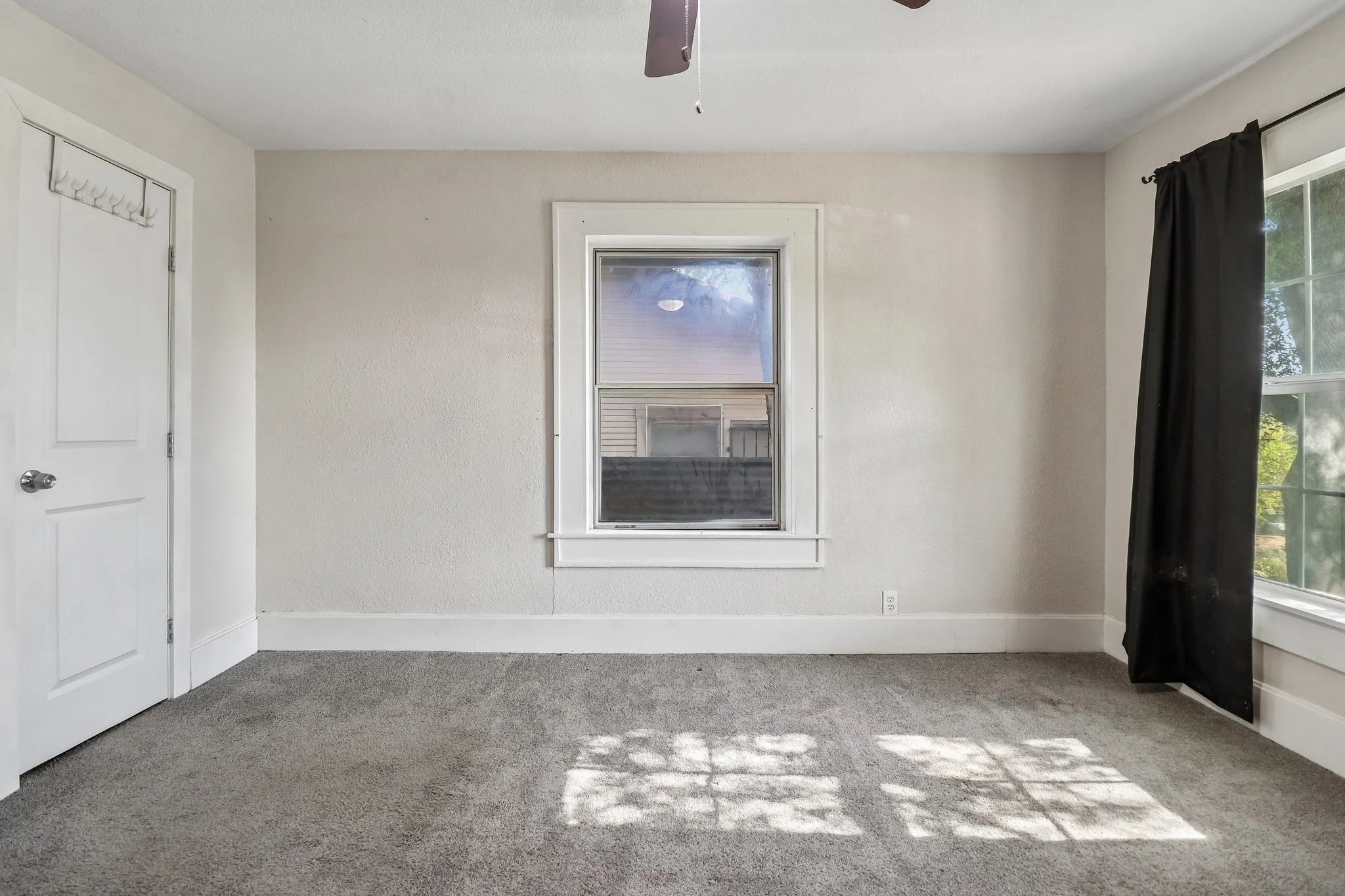 Gray carpet flooring, white walls, white trim, multiple windows with natural light, and a ceiling fan