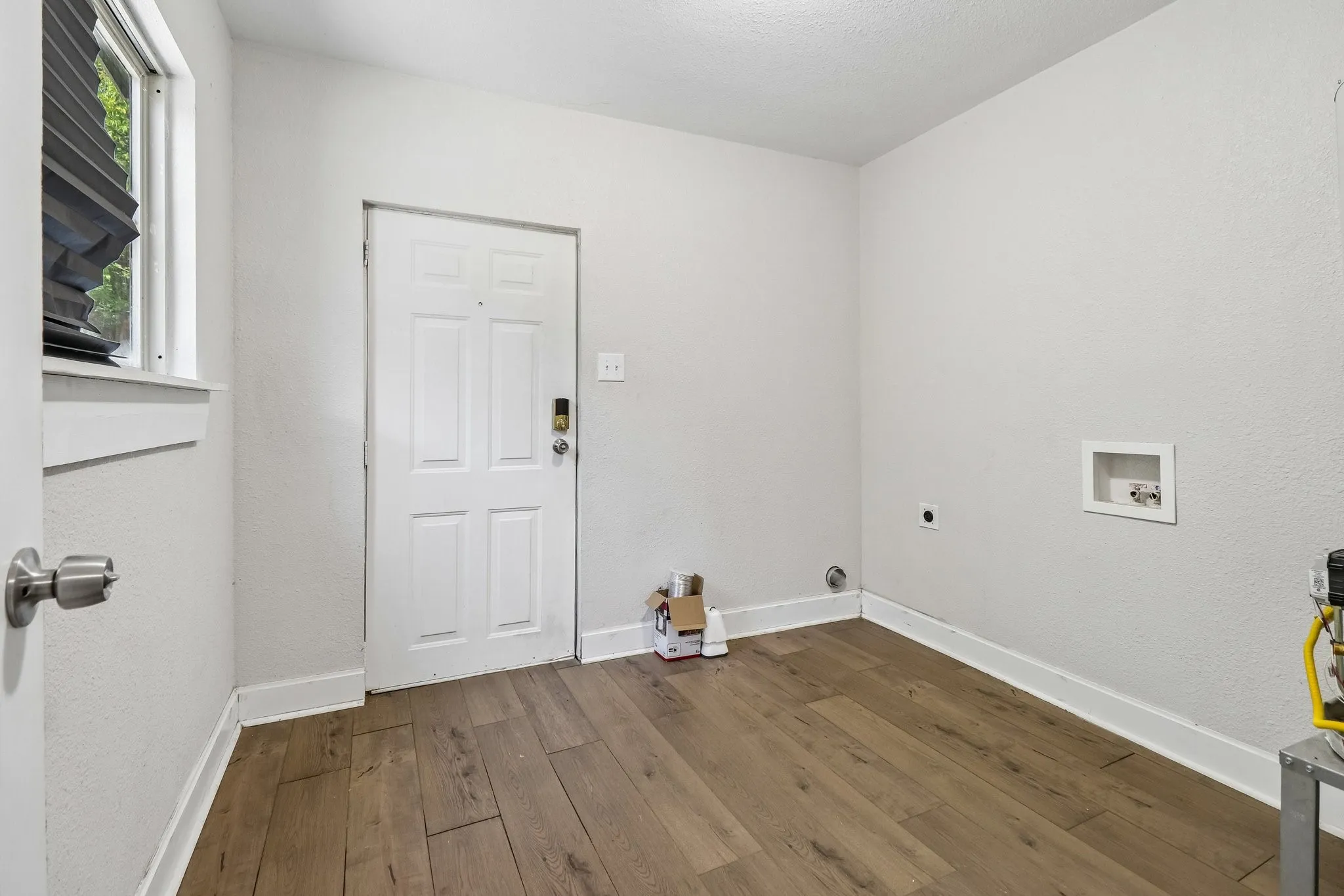 Wood-finish flooring with white trim, a window with horizontal blinds, and a white paneled door