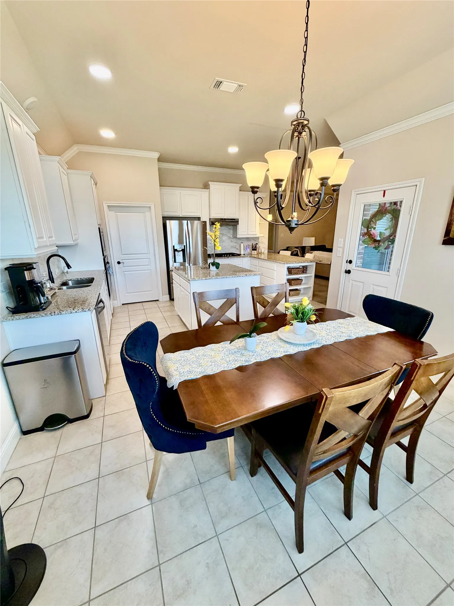 Open-concept kitchen and dining area featuring white cabinetry, a kitchen island with a granite countertop, a tile backsplash, and tile flooring