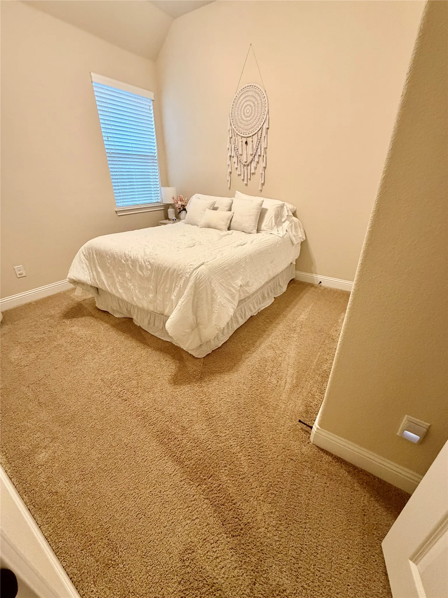 Recessed window with blinds, vaulted ceiling, and neutral carpet flooring