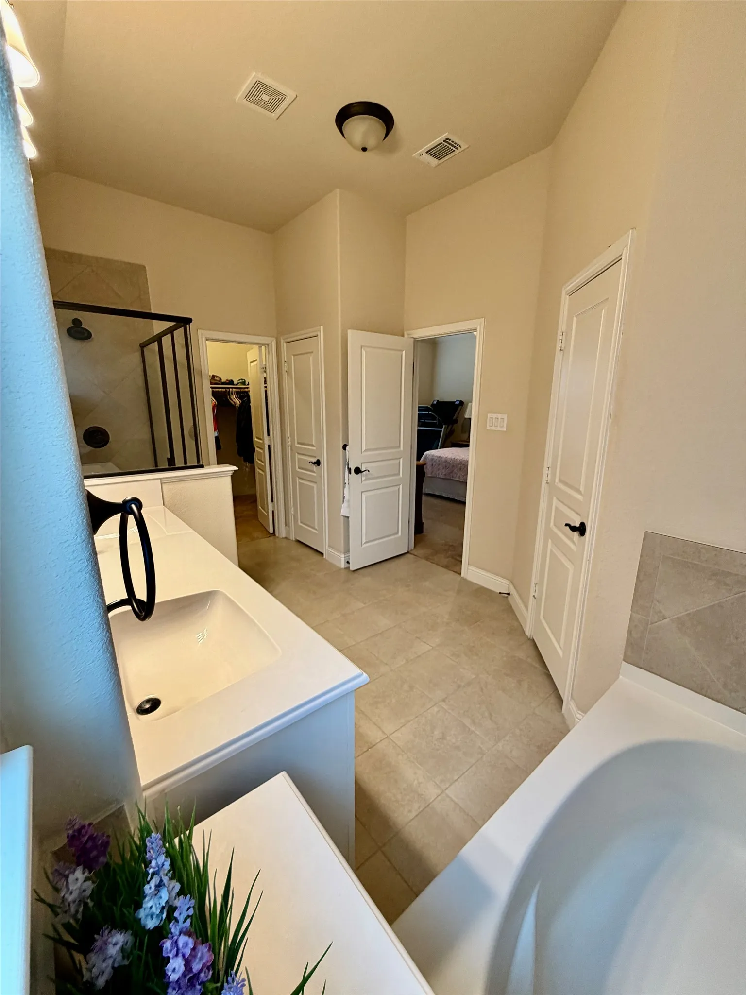 Double vanity with integrated sinks, walk-in shower with glass enclosure, separate soaking tub, and tile flooring