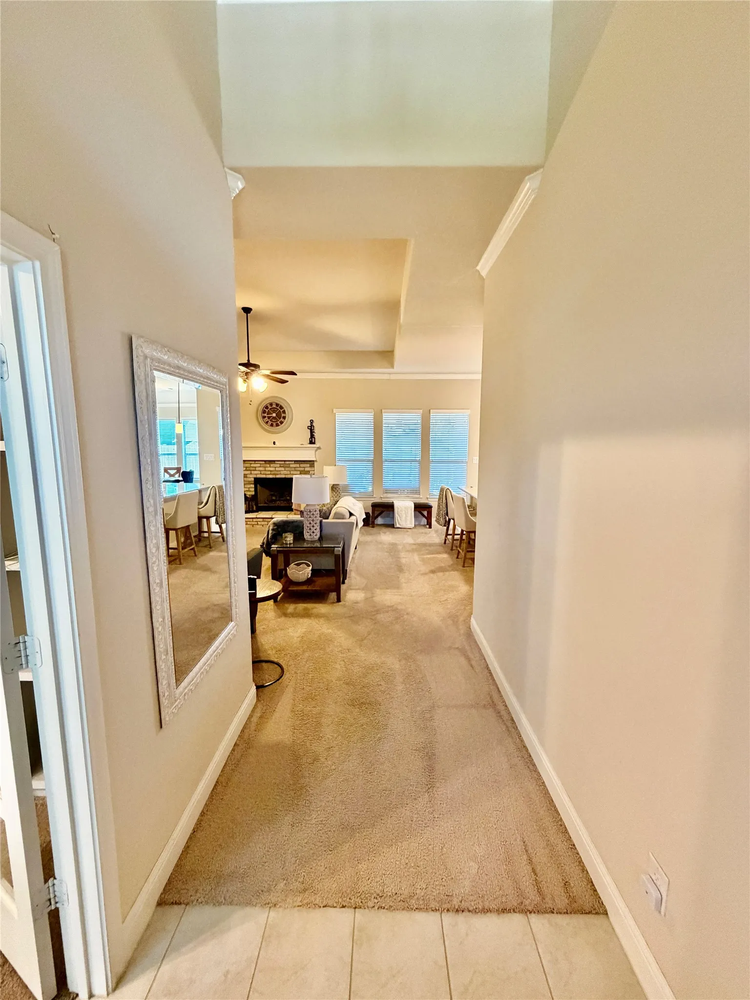 Hallway with tile flooring transitioning to carpet, crown molding, and an open concept living space