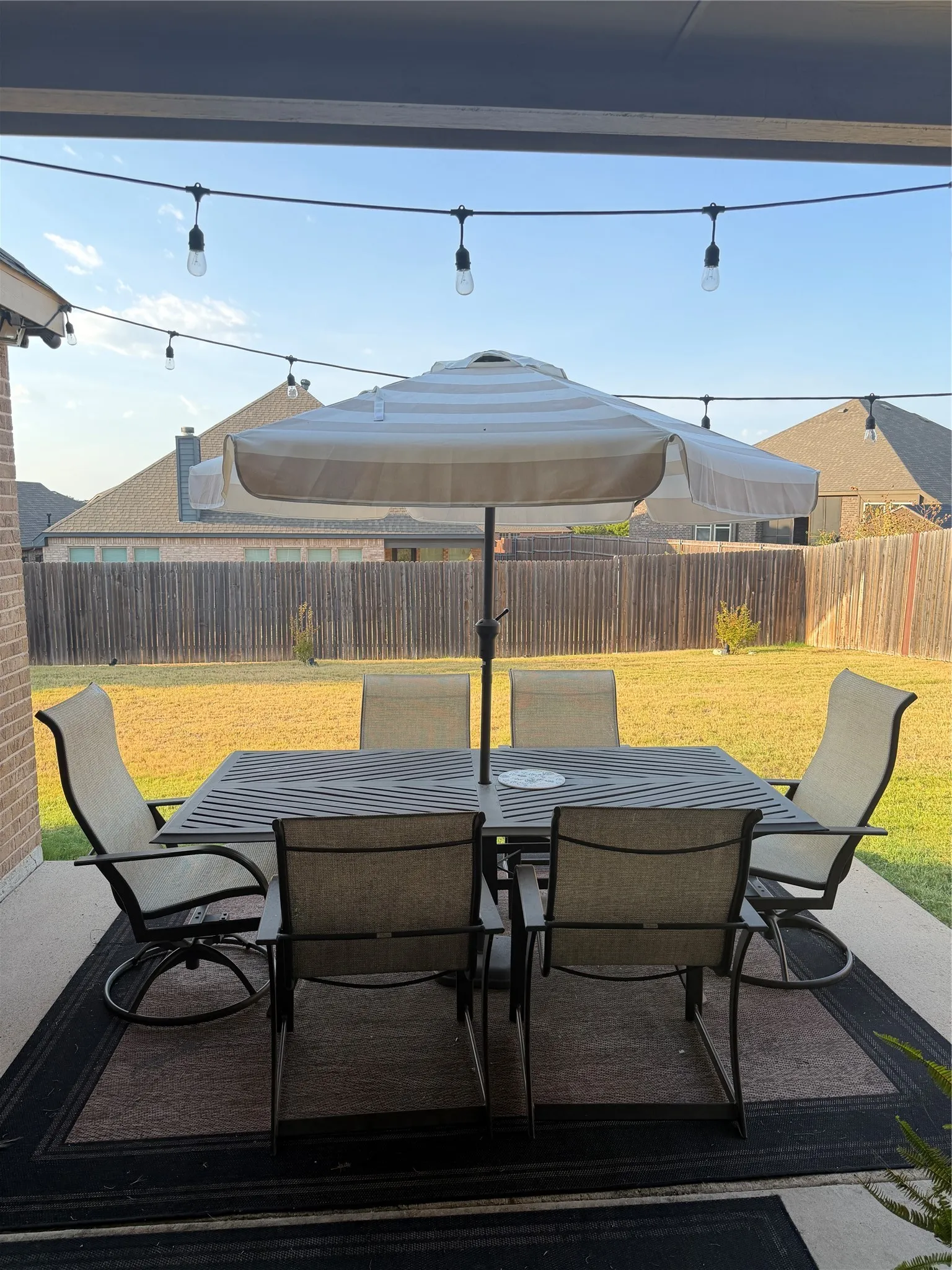 Covered patio area with concrete flooring, string lighting, and a wooden privacy fence