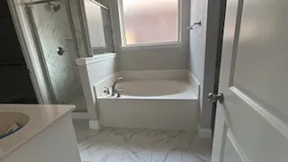 Built-in soaking tub with deck-mounted faucet, glass-enclosed shower with tile surround, and white vanity with an undermount sink