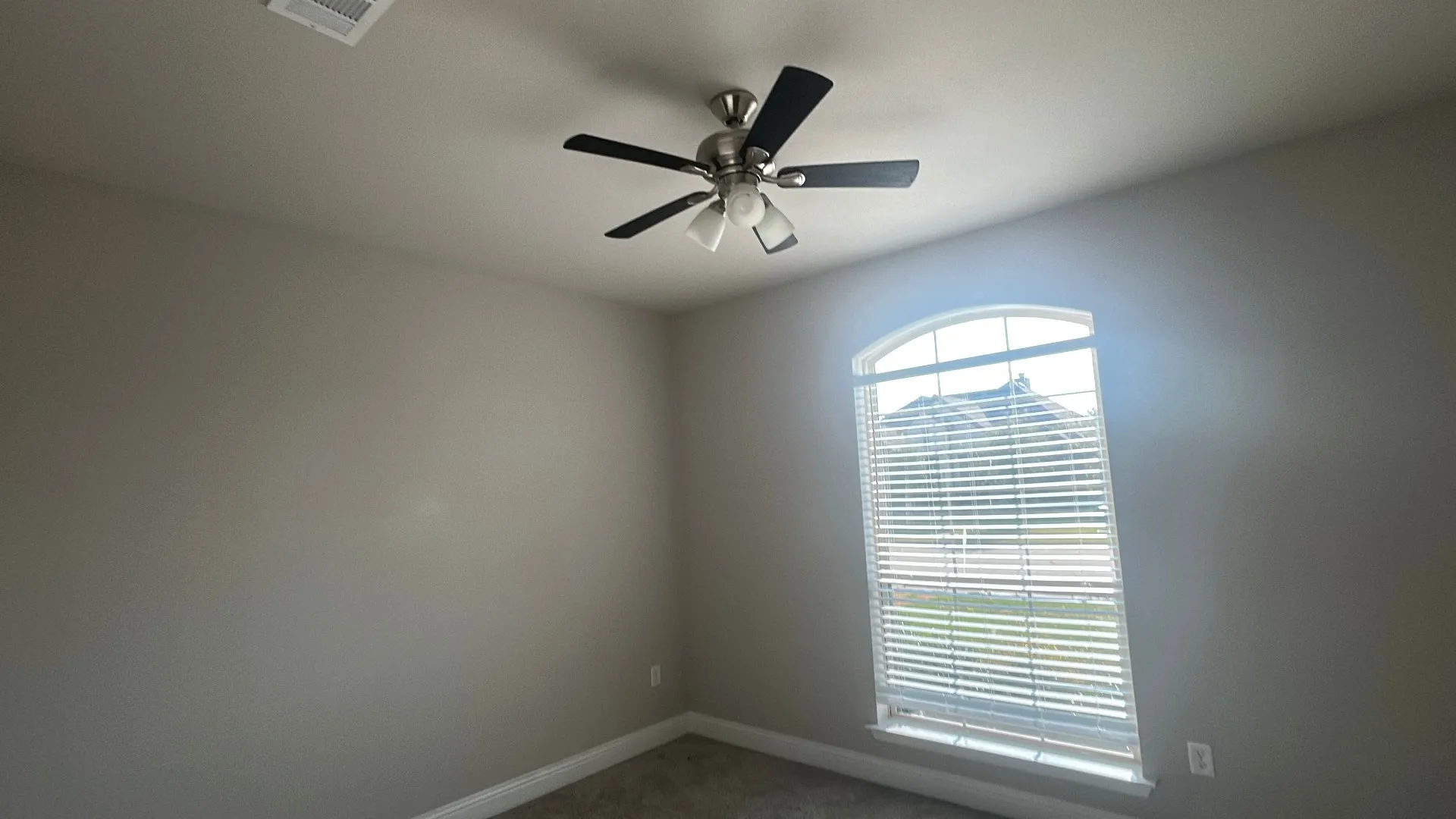 Arched window with blinds, ceiling fan with light fixture, light gray wall paint, and gray carpet