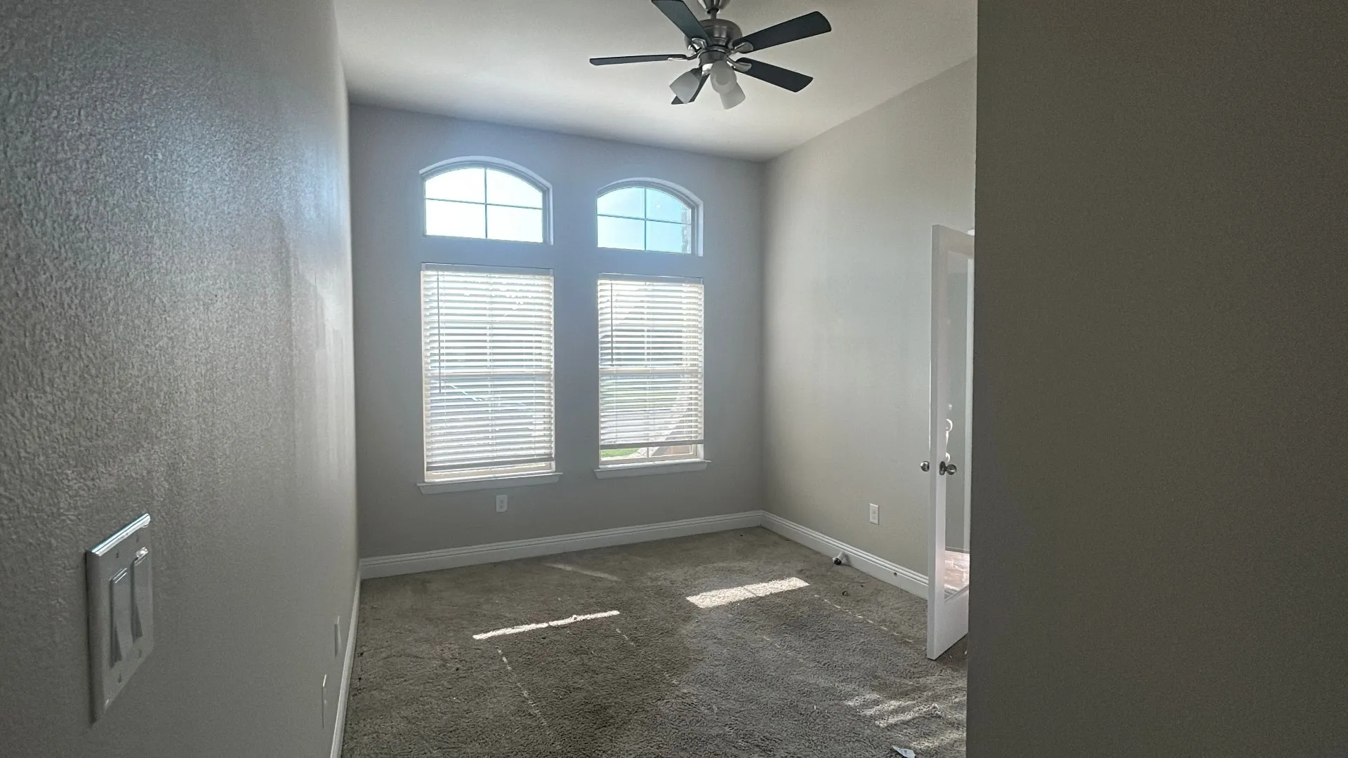Dual arched windows with blinds, ceiling fan with integrated lighting, and neutral wall tones