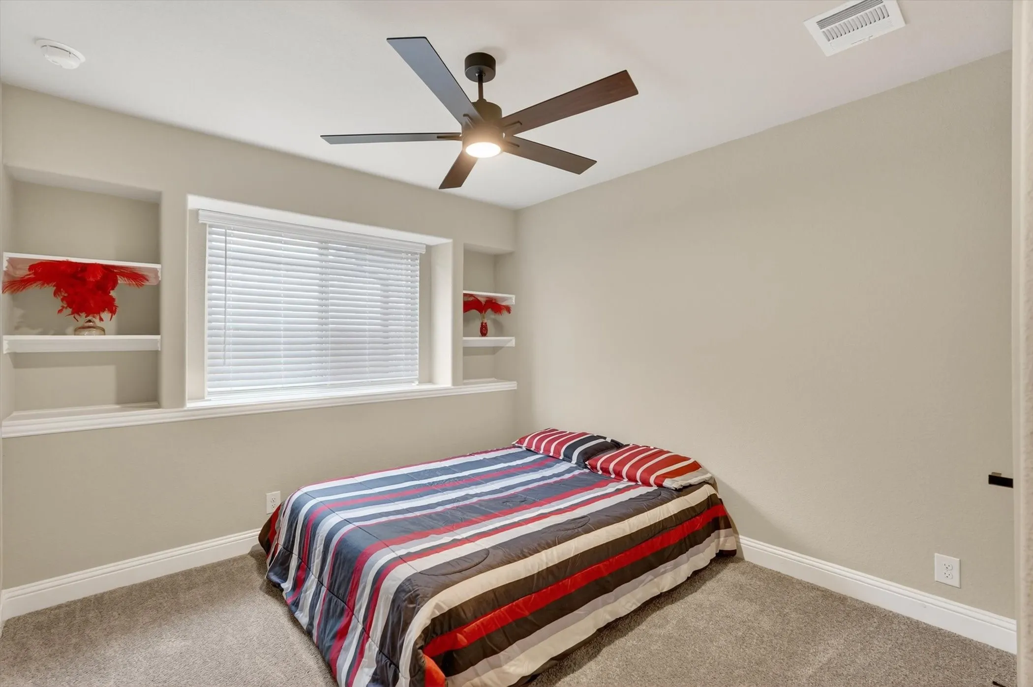Bright secondary bedroom featuring carpet flooring, a ceiling fan with integrated lighting, and built-in shelving with display alcoves