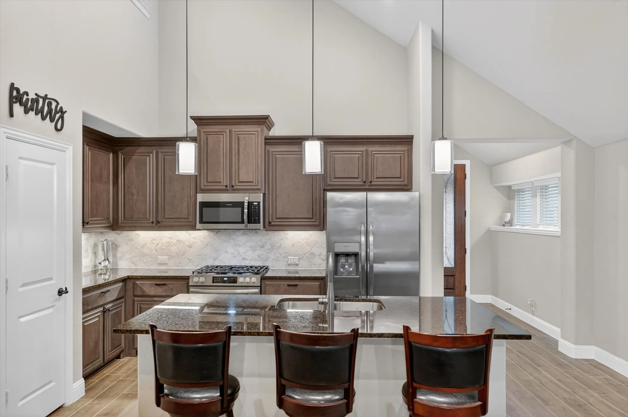 Kitchen featuring vaulted ceilings, wood-finish flooring, stainless steel appliances, a center island with bar seating, and dark wood cabinetry
