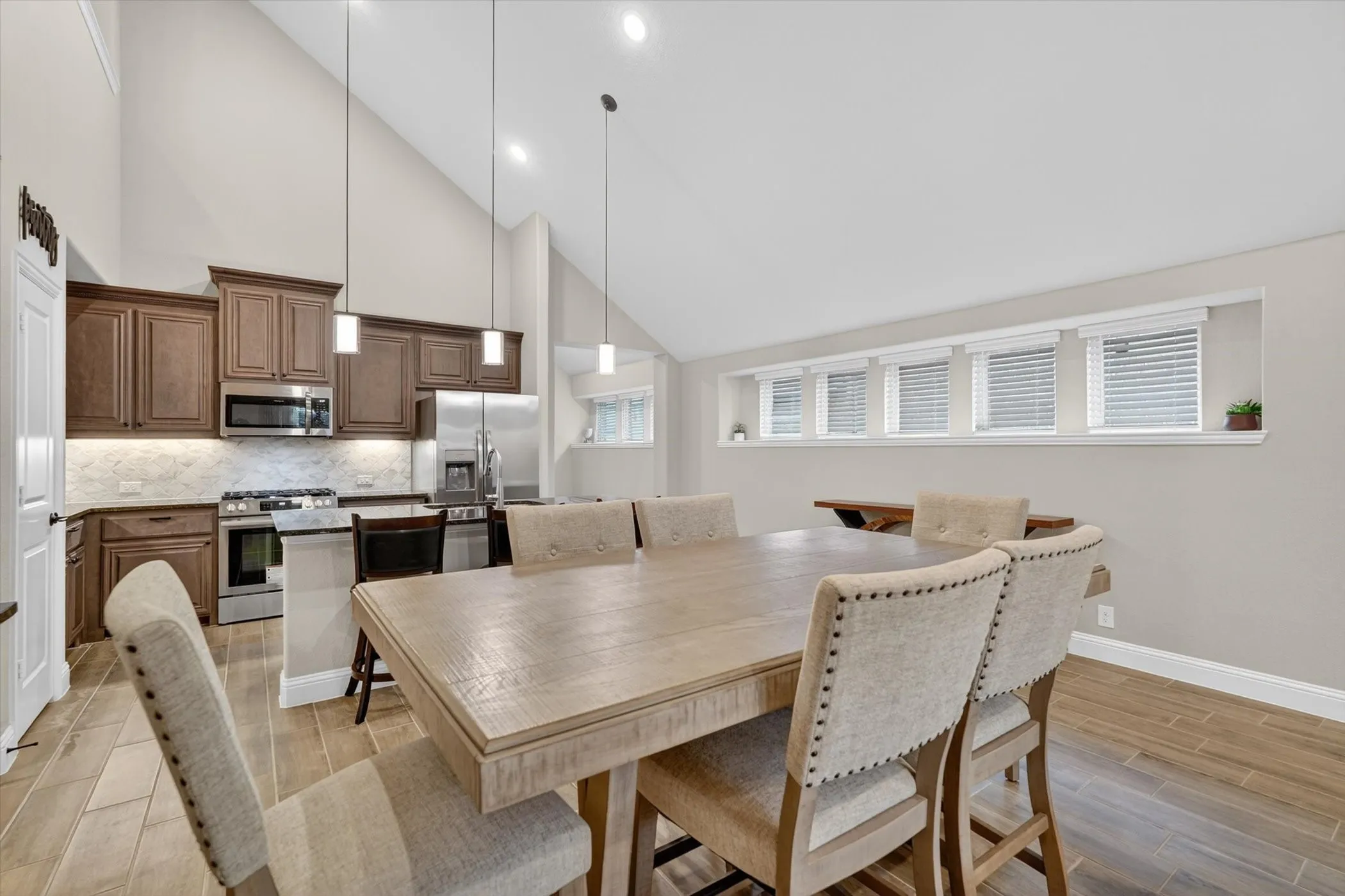 Kitchen and dining area featuring wood-finish flooring, vaulted ceilings, pendant lighting, stainless steel appliances, and a tiled backsplash