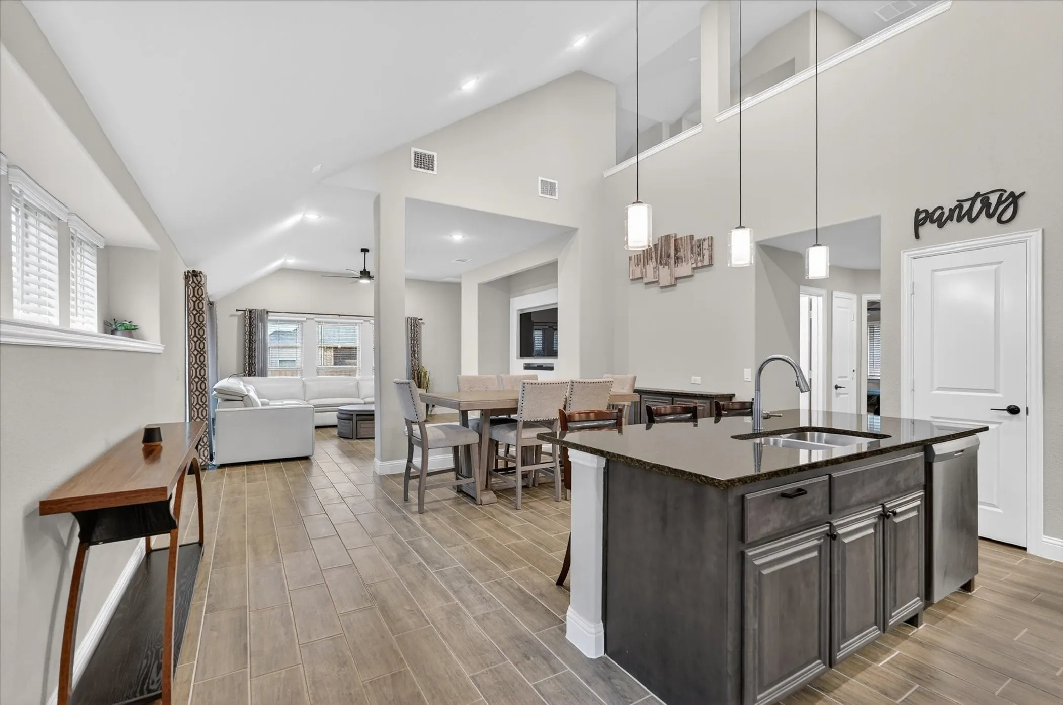 Vaulted ceilings, wood-finish flooring, kitchen island with sink, stainless steel dishwasher, and contemporary pendant lighting