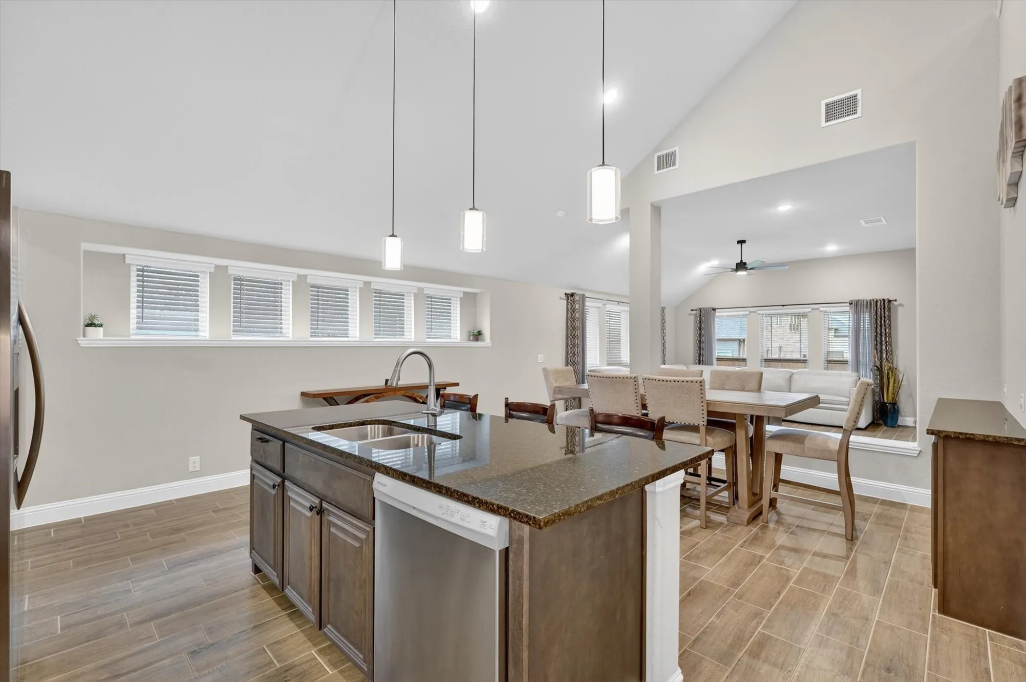 Kitchen island with double basin sink, dark cabinetry, and integrated dishwasher