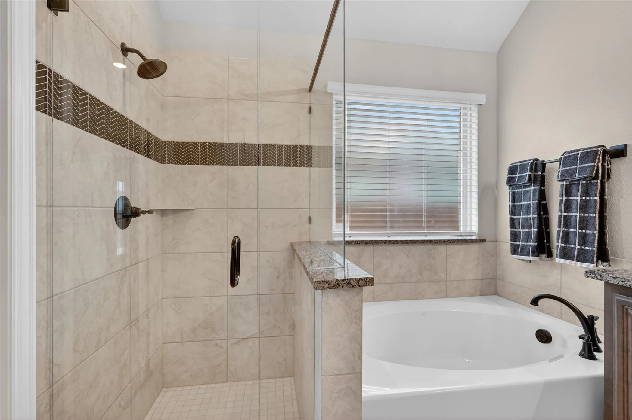 Glass-enclosed shower with decorative tile accent, separate soaking tub, and bronze-finish fixtures